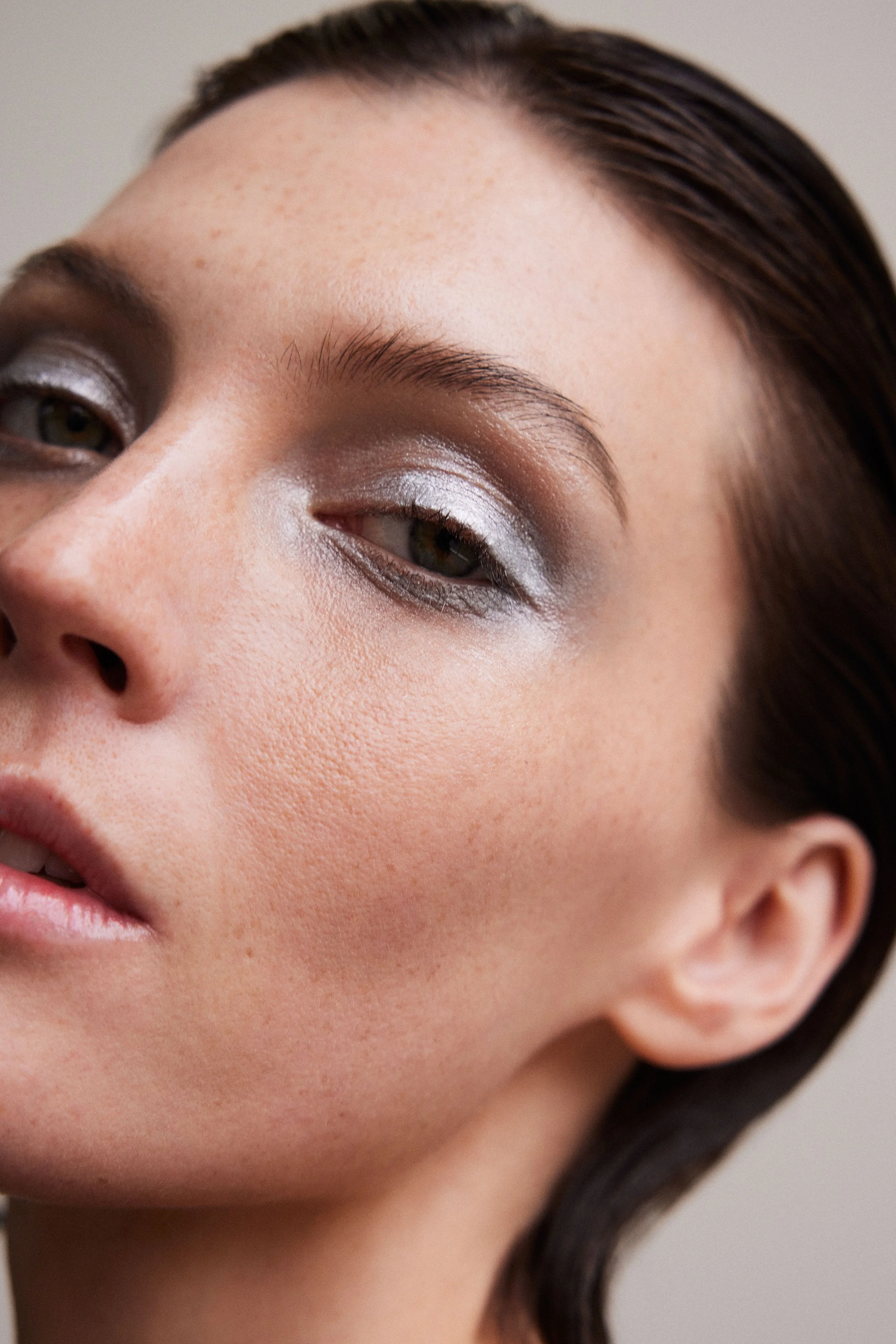 Close-up of a woman's face showcasing silver eye makeup and natural skin texture.