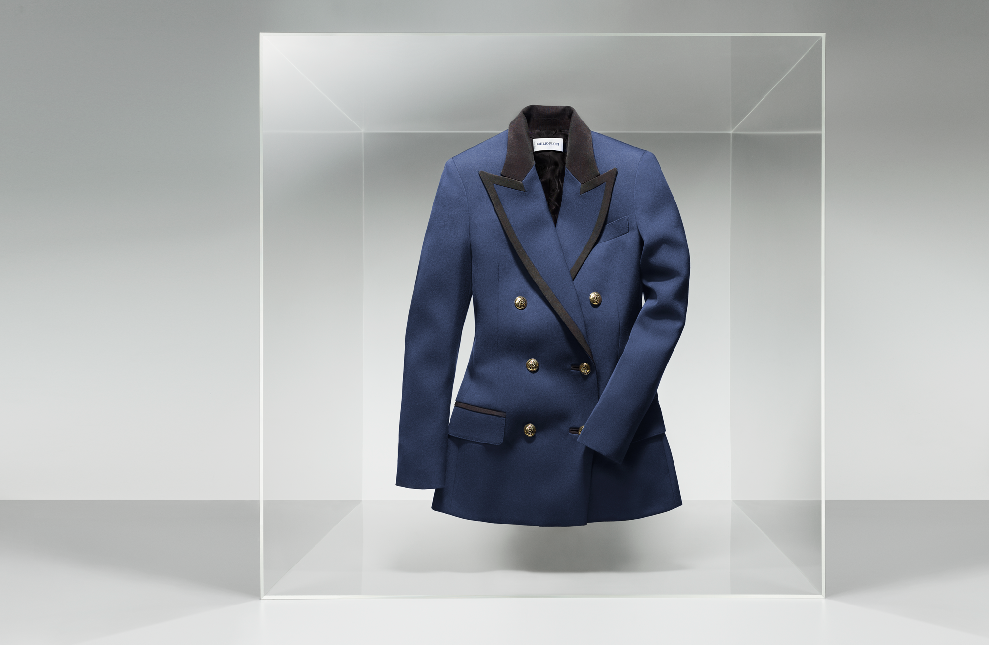 A blue double-breasted blazer with black lapels displayed inside a glass box.