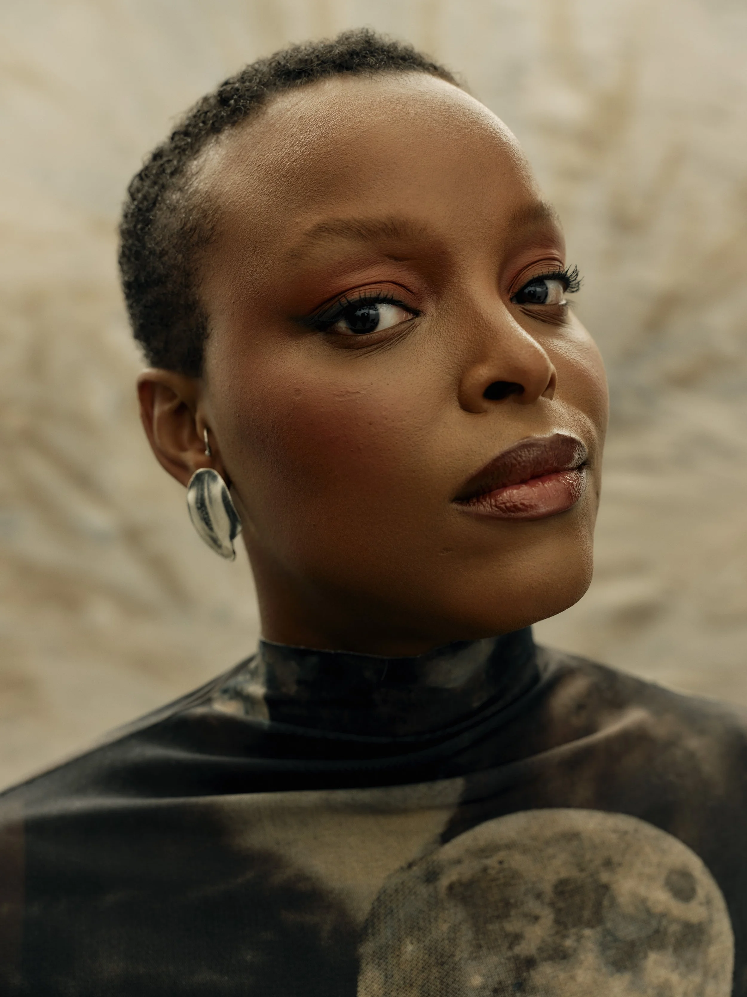 A woman with short hair, wearing earrings and a black turtleneck shirt with a moon print.