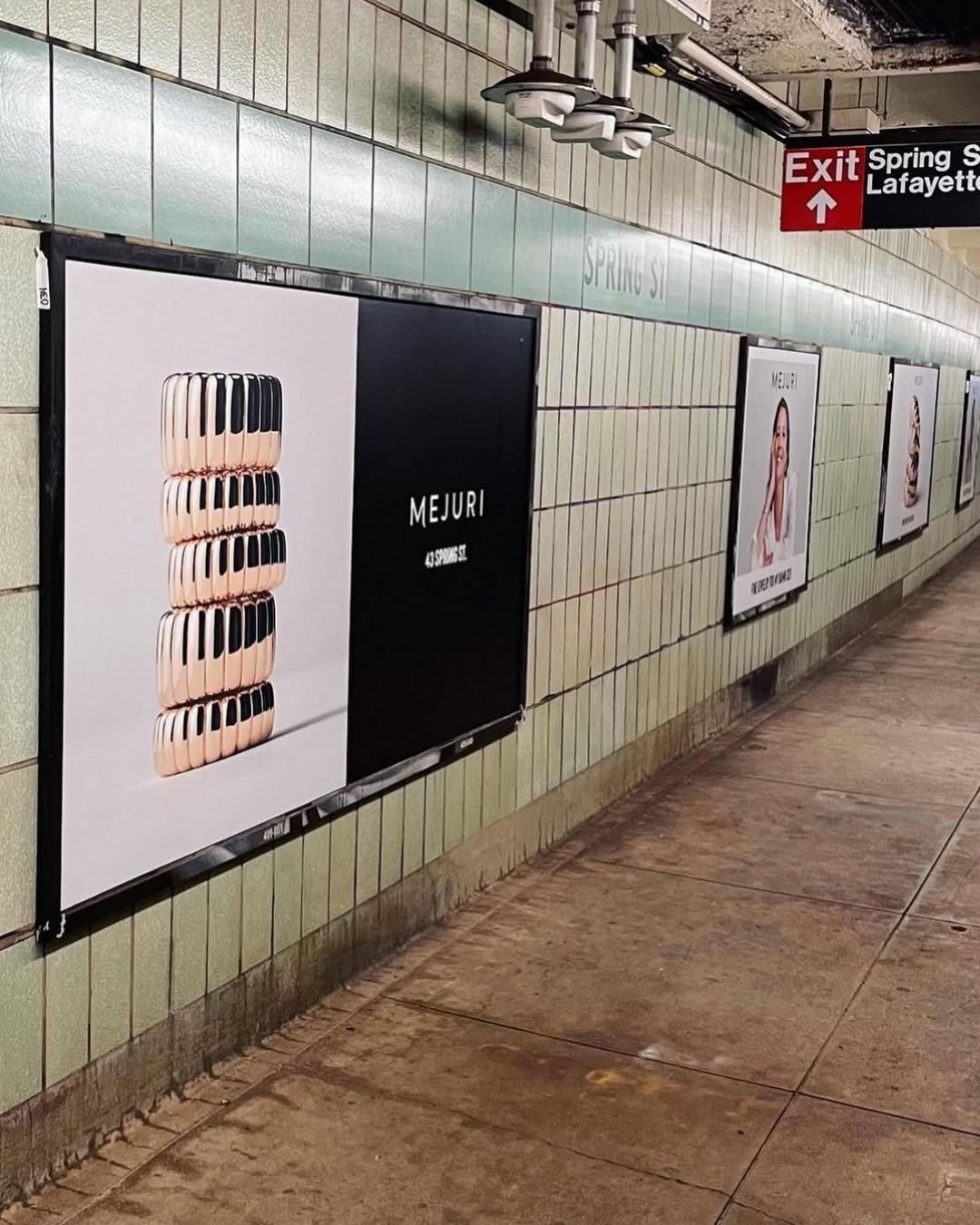 Advertising posters on a subway station wall, one promoting a mobile phone with a stack of phones imagery, others featuring women, and a sign indicating an exit towards Lafayette Square.