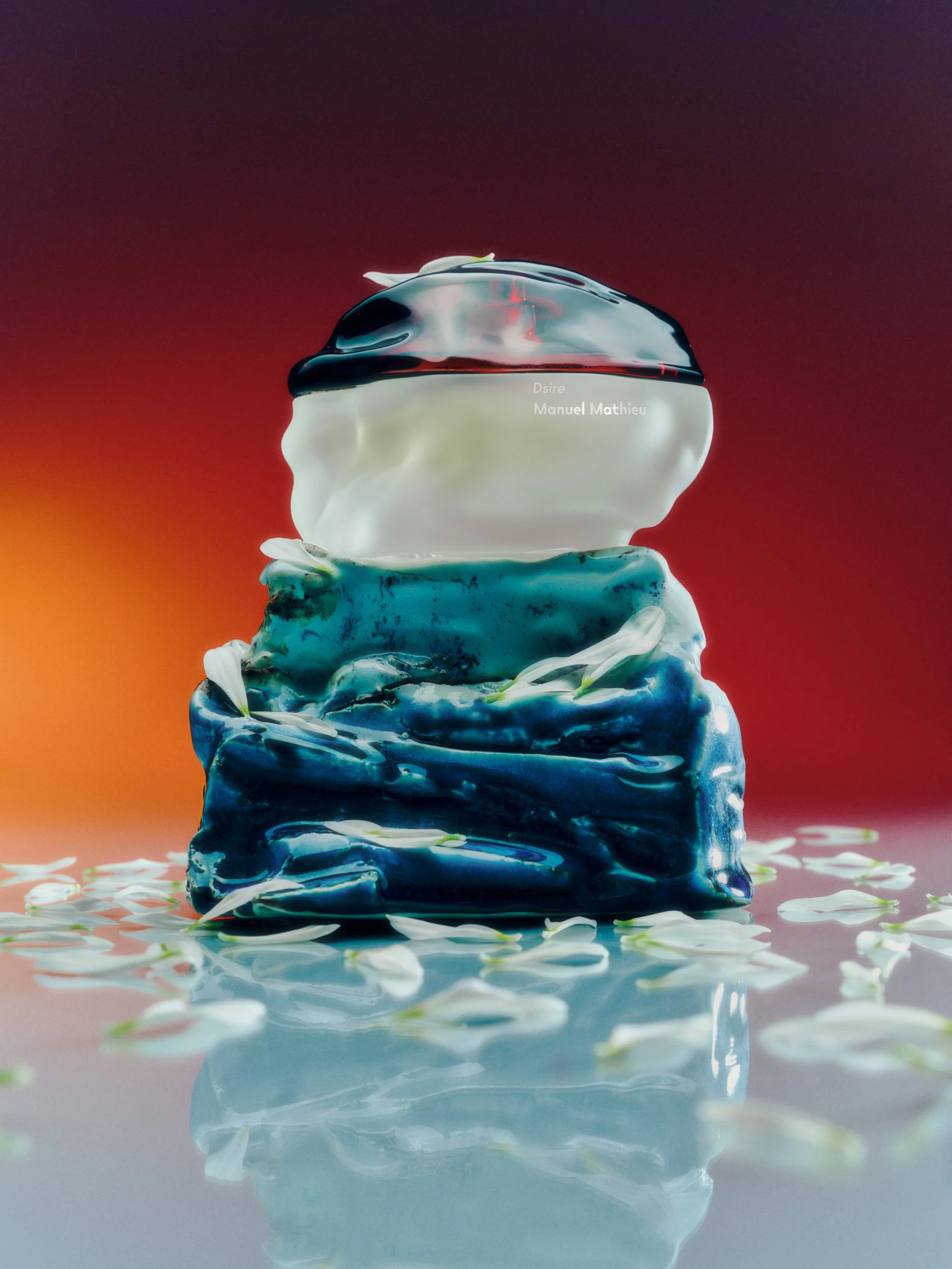 Abstract sculpture with layered, textured shapes in blue, white, and clear materials, topped with a clear, rounded form, surrounded by scattered white petals and reflected on a glossy surface with a gradient red to orange background.