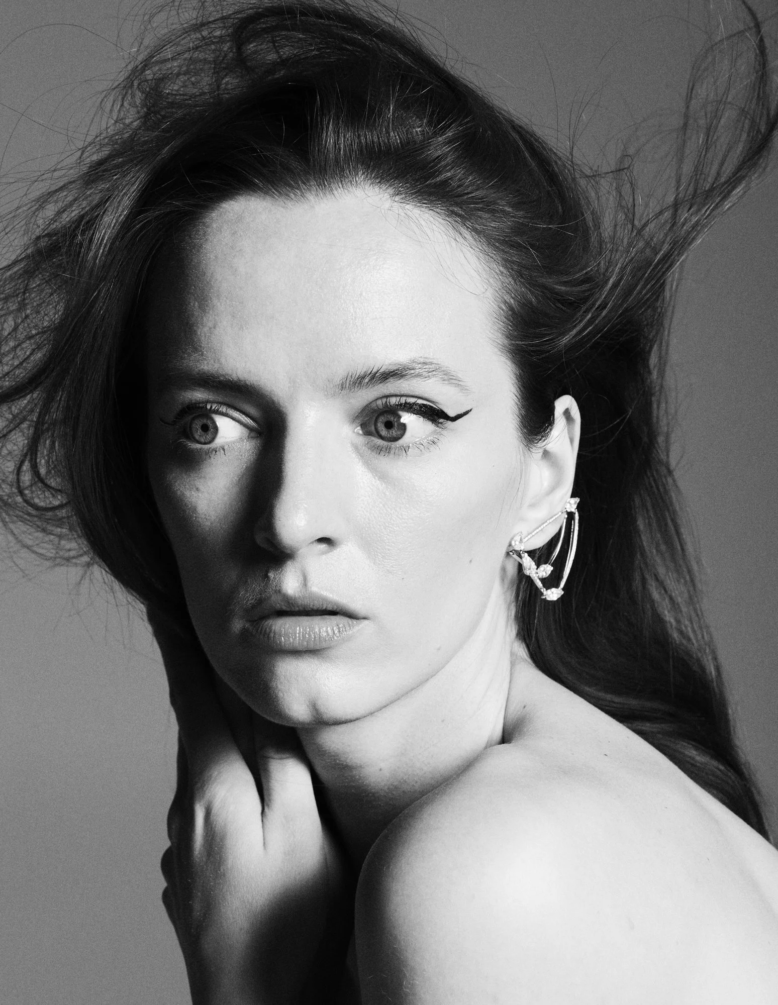 Black and white portrait of a woman with voluminous hair, wearing earrings, looking to the side with a serious expression.
