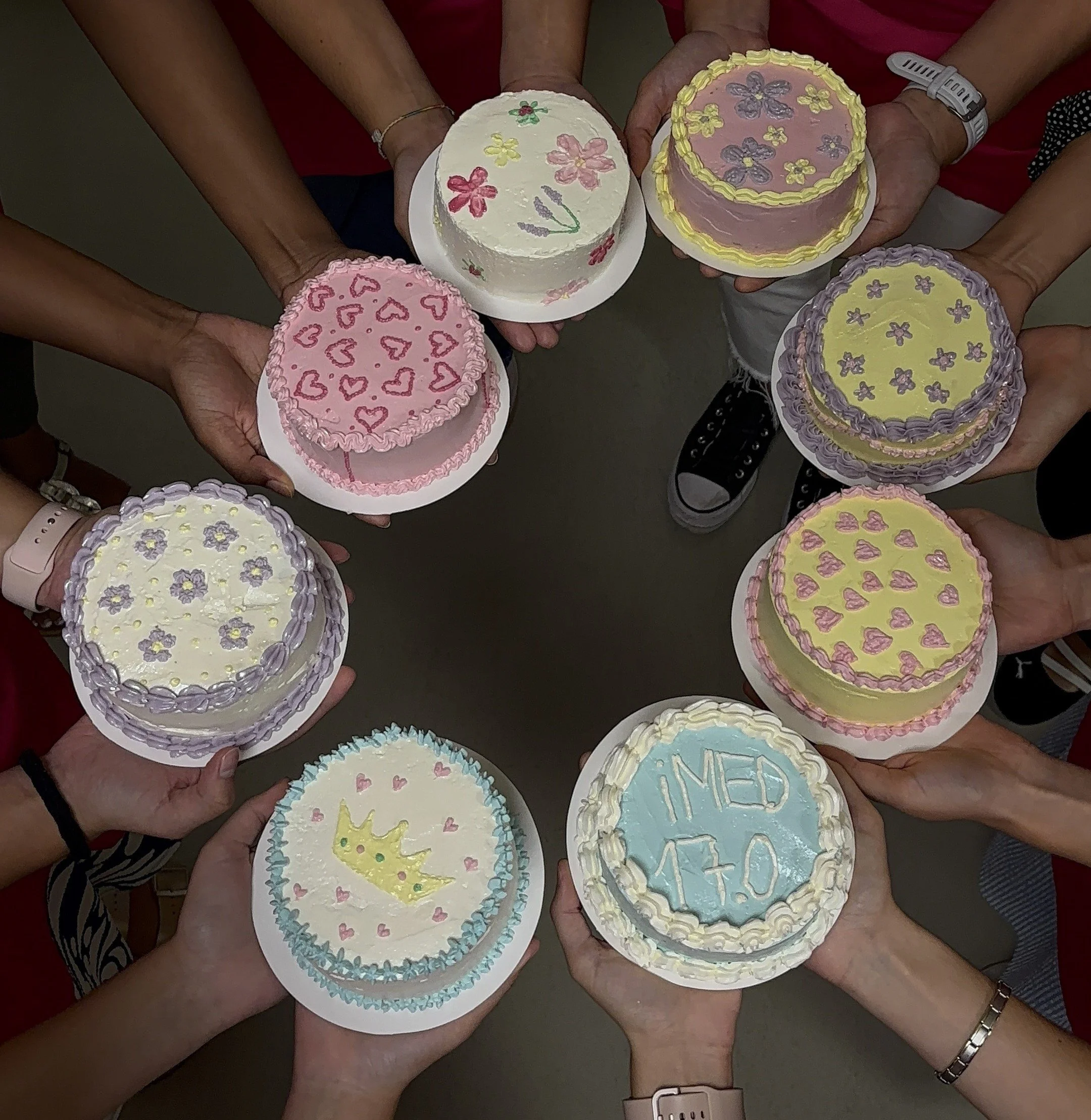 Several people holding decorated cakes with pastel colors, flowers, hearts, and a crown, celebrating a medical graduation or achievement.