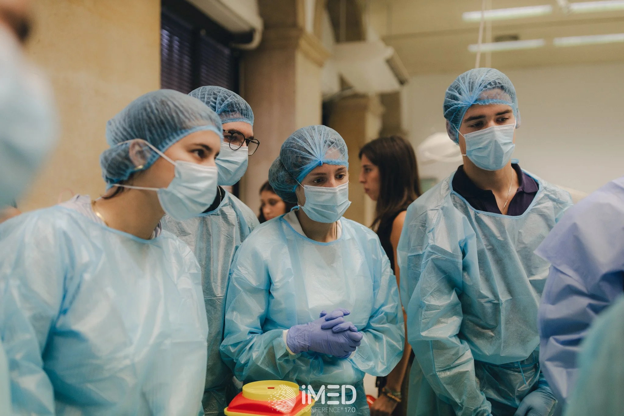 Group of healthcare professionals wearing surgical masks, gowns, and hair covers during a medical conference.