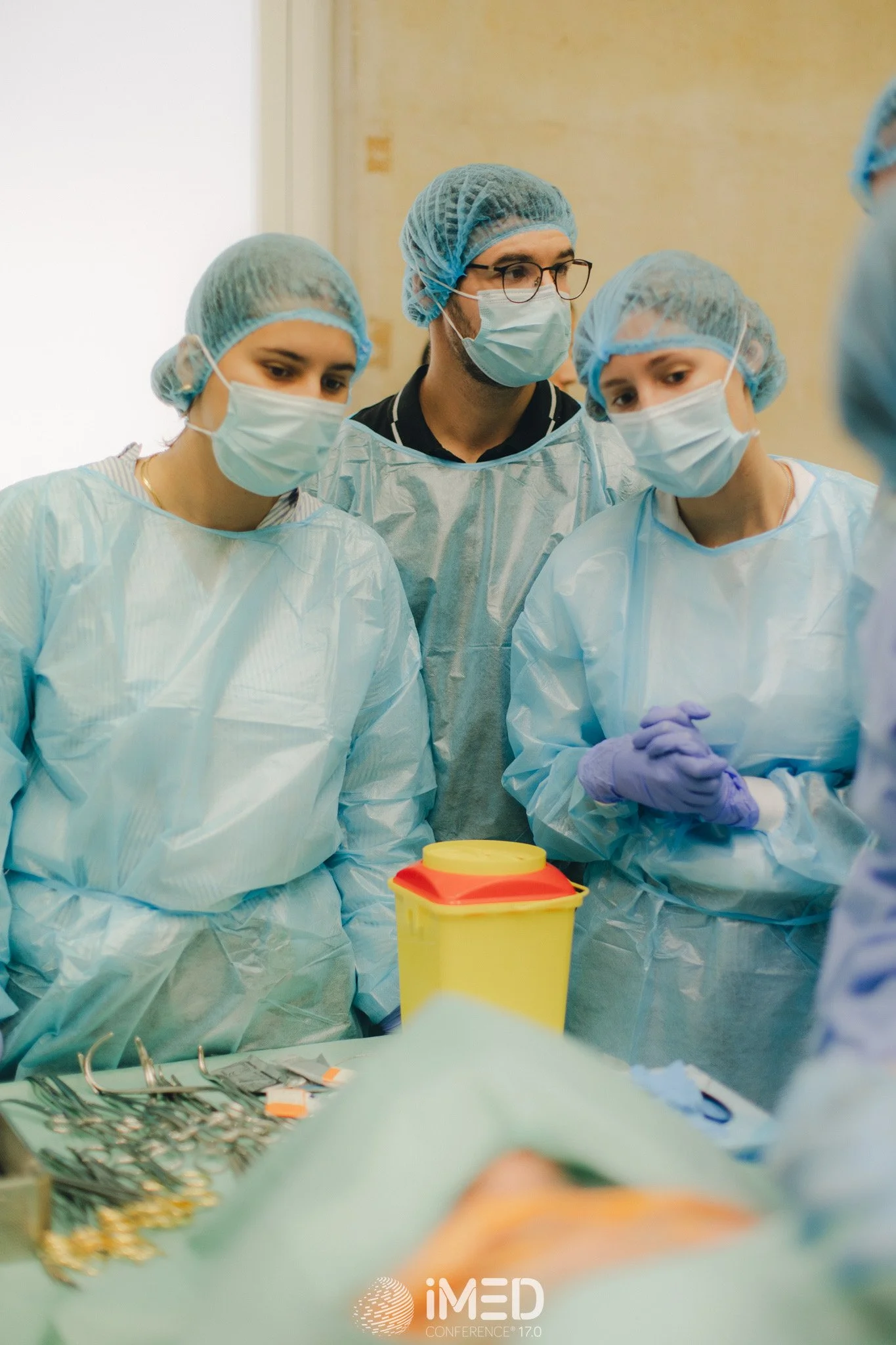 Group of surgeons in surgical masks, gowns, and hair covers gathered around an operating table during surgery.