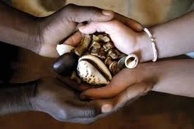 Two hands, one dark-skinned and one light-skinned, holding a collection of seashells together.