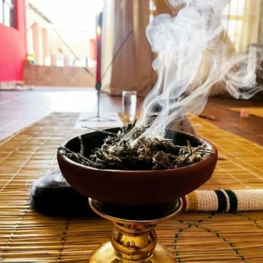 Incense burning on a wooden table with smoke rising, indoors with sunlight filtering through the windows.
