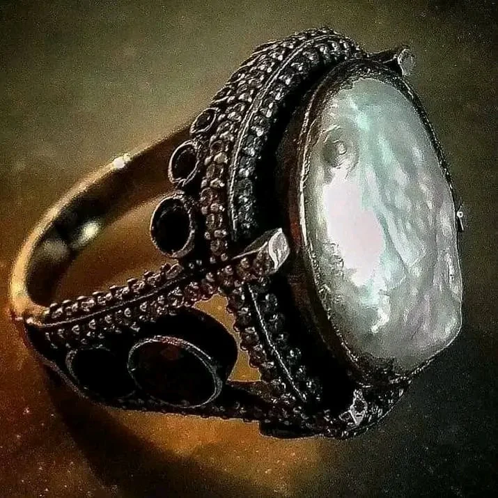 A vintage silver ring with an oval-shaped white gemstone and black decorative details.