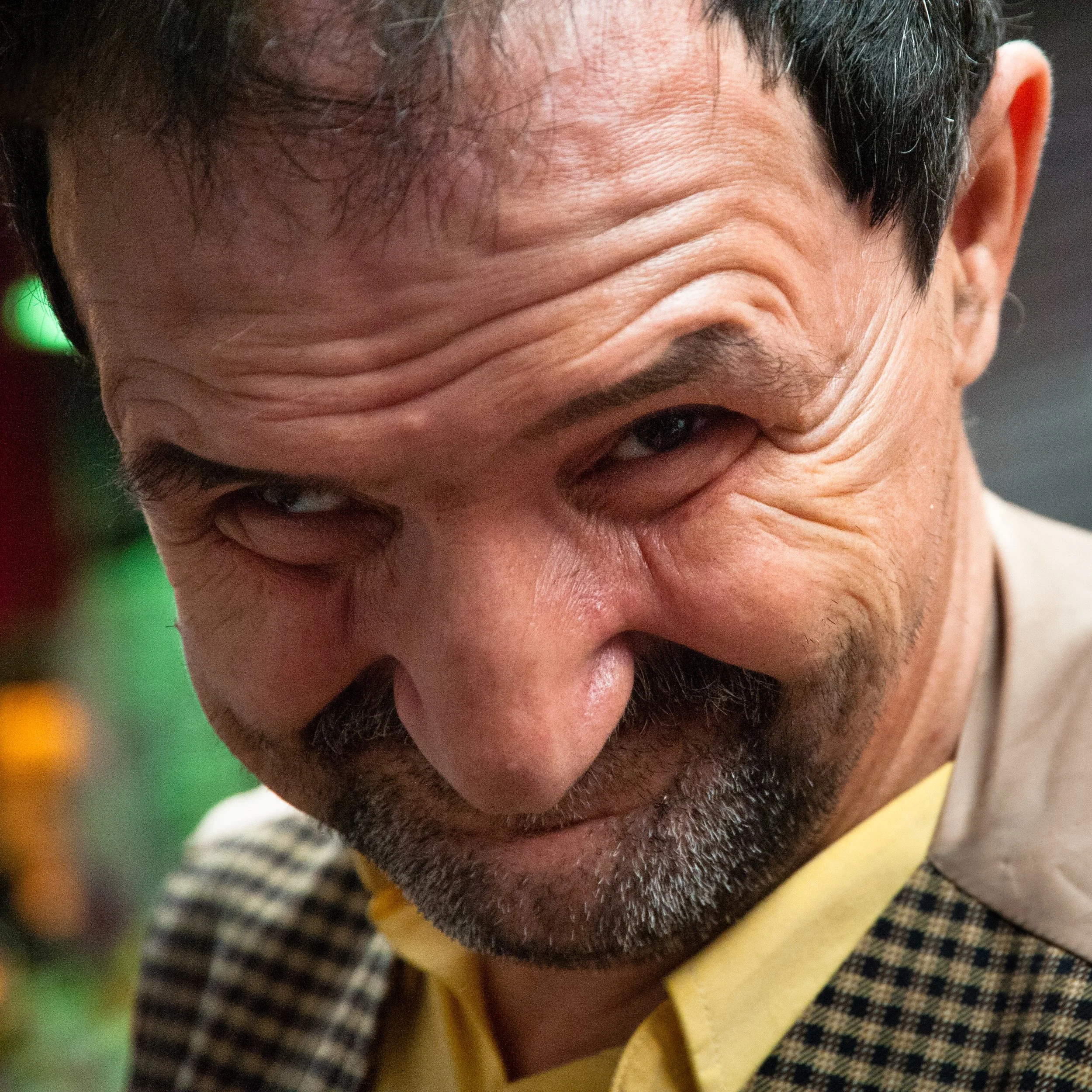 Close-up of a middle-aged man with a playful facial expression, slightly squinting one eye, and wearing a yellow shirt.