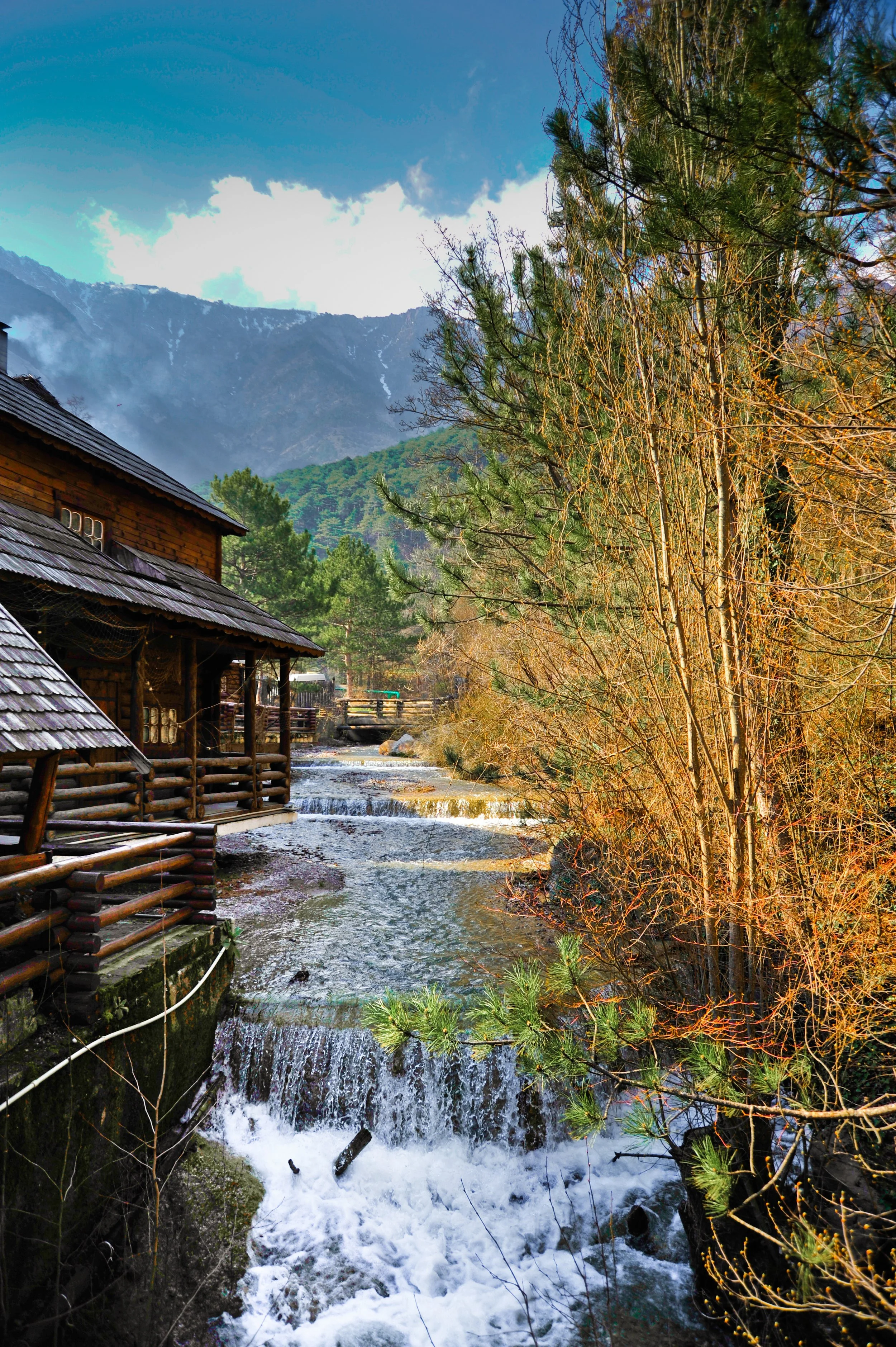 A mountain stream flowing beside wooden cabins with a forested mountain backdrop.