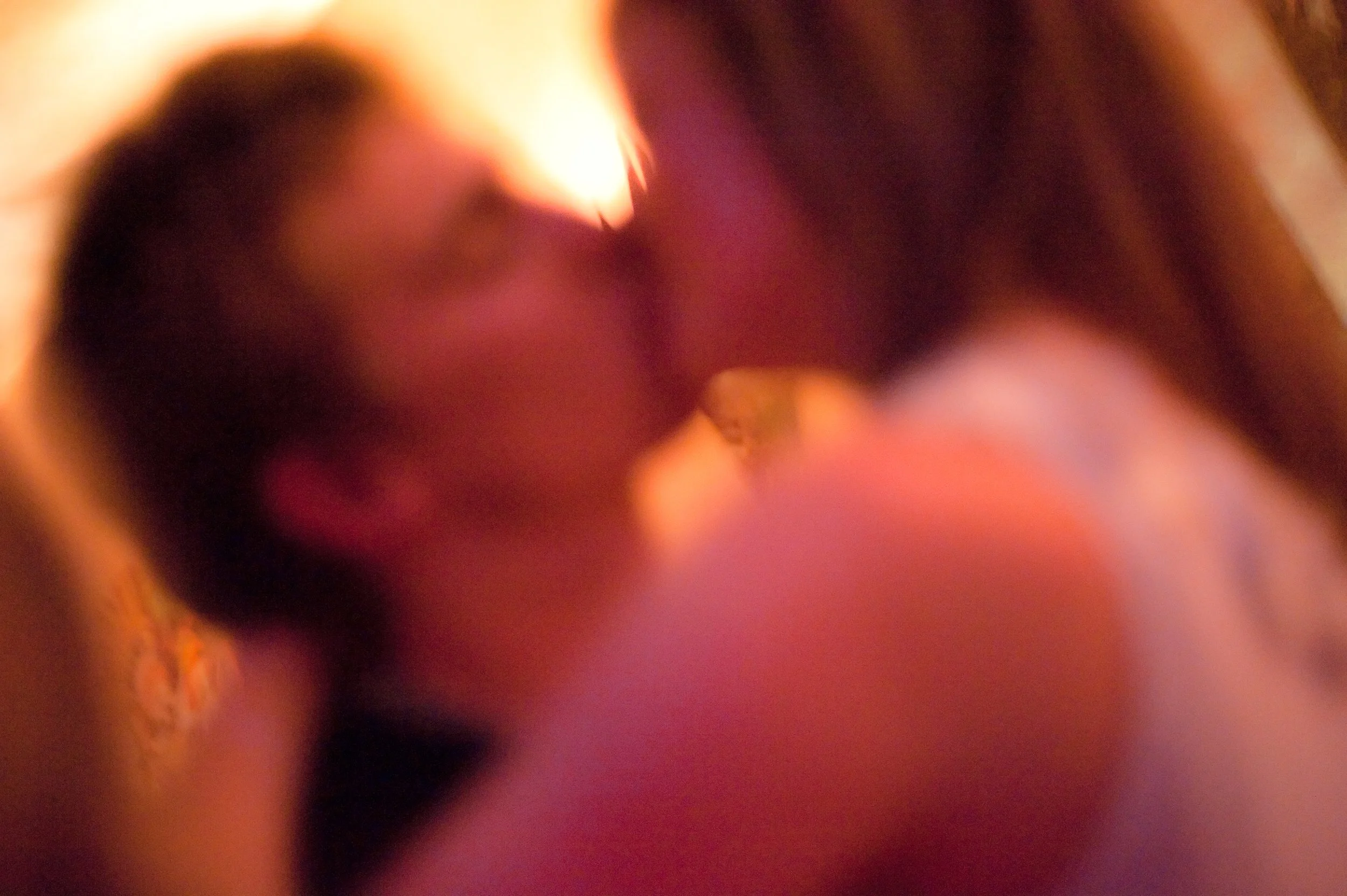 A blurred close-up photo of two people kissing, with warm, dim lighting.