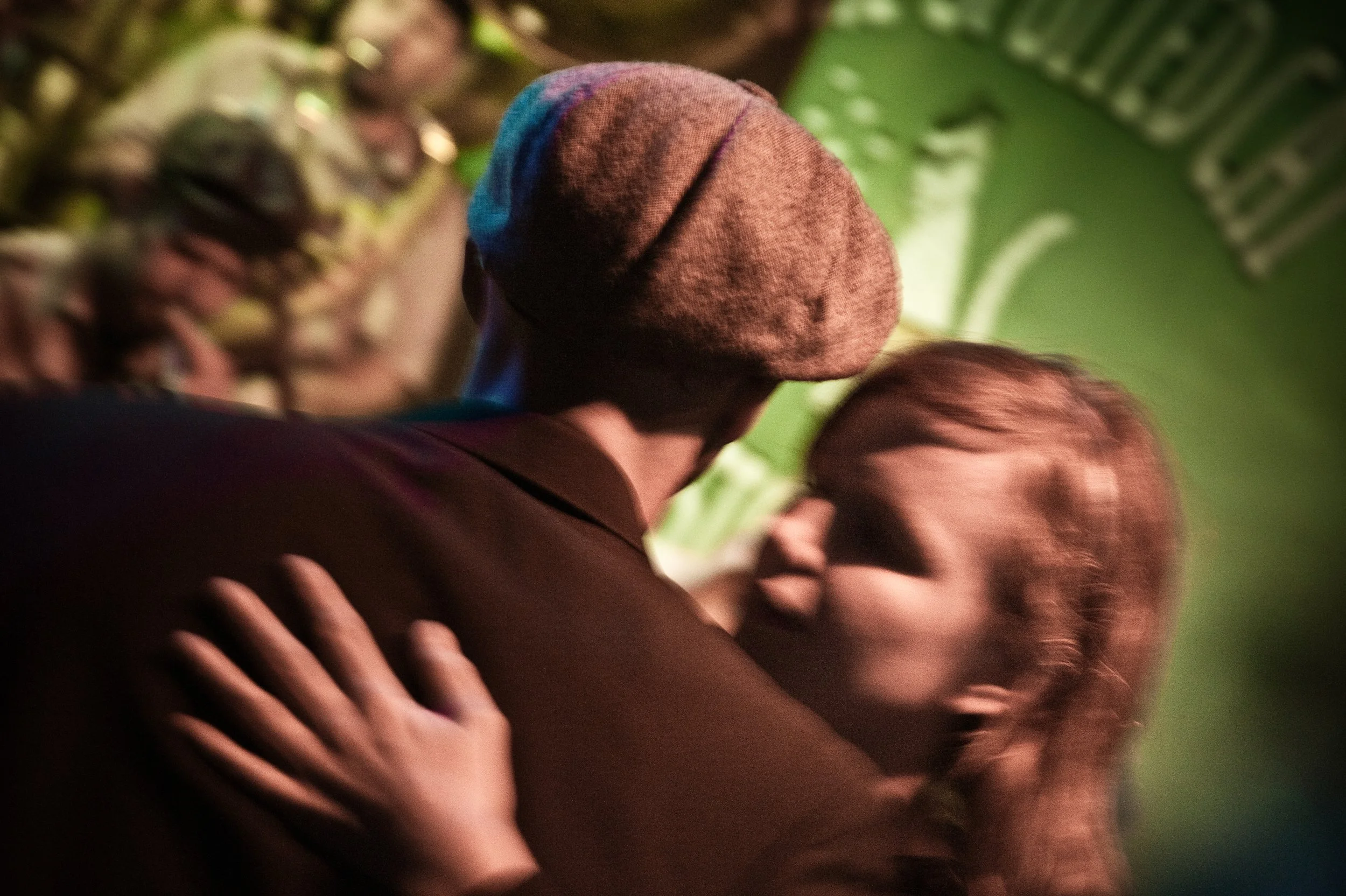 A couple sharing a kiss, with the woman in focus and the man in a brown coat and a gray hat.
