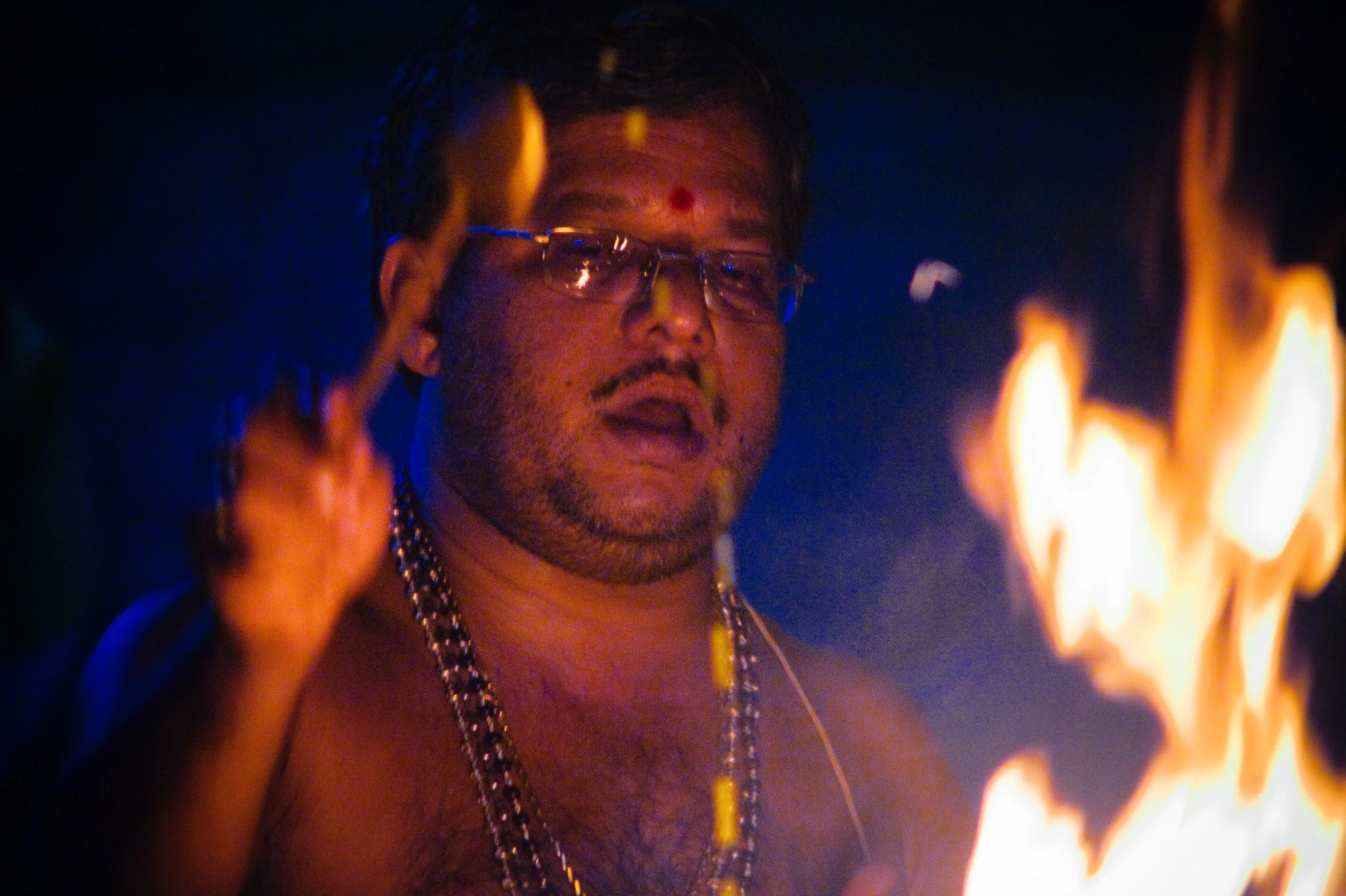 Man with glasses and jewelry near a fire at night