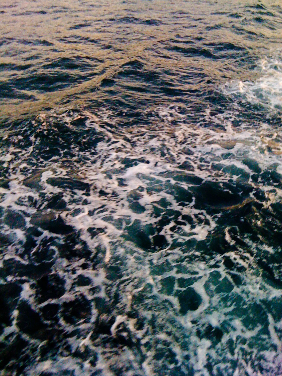 Close-up of ocean water with waves and white foam at sunset or sunrise.