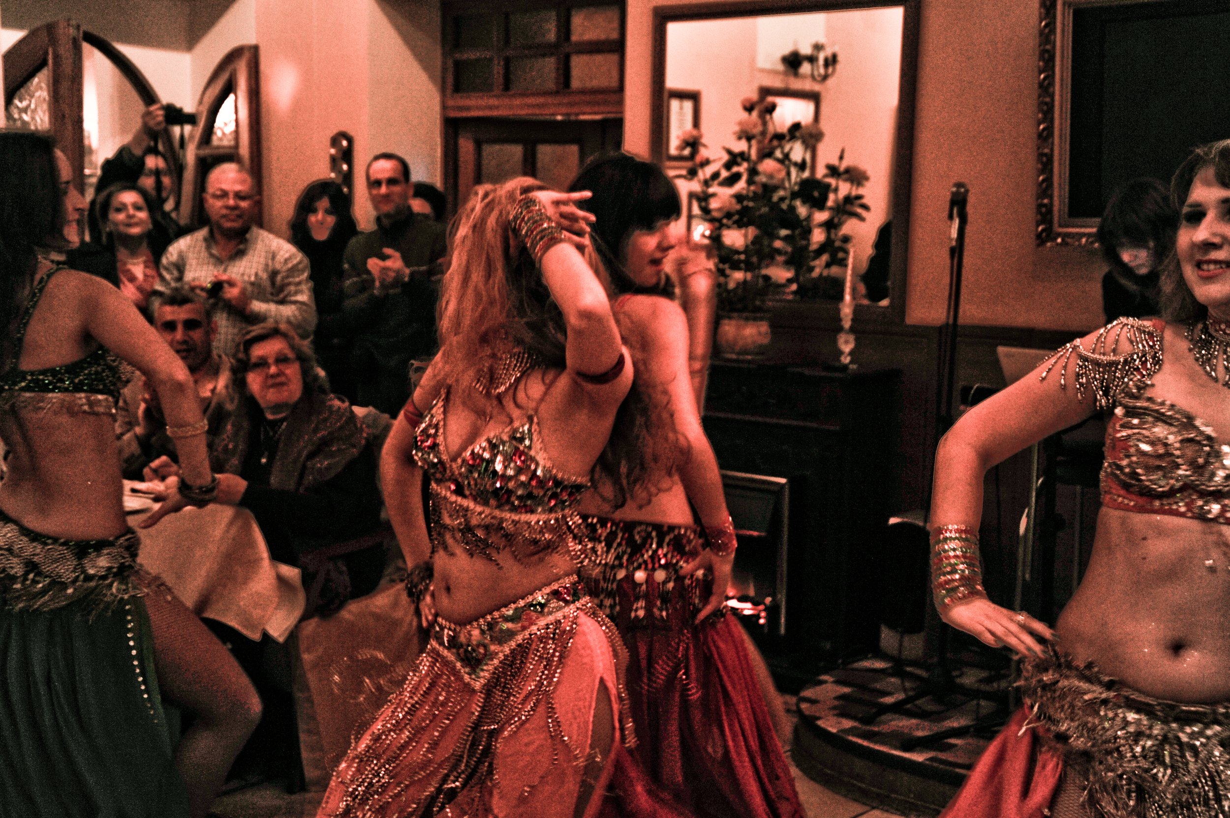 Women performing a belly dance in a restaurant with an audience watching.