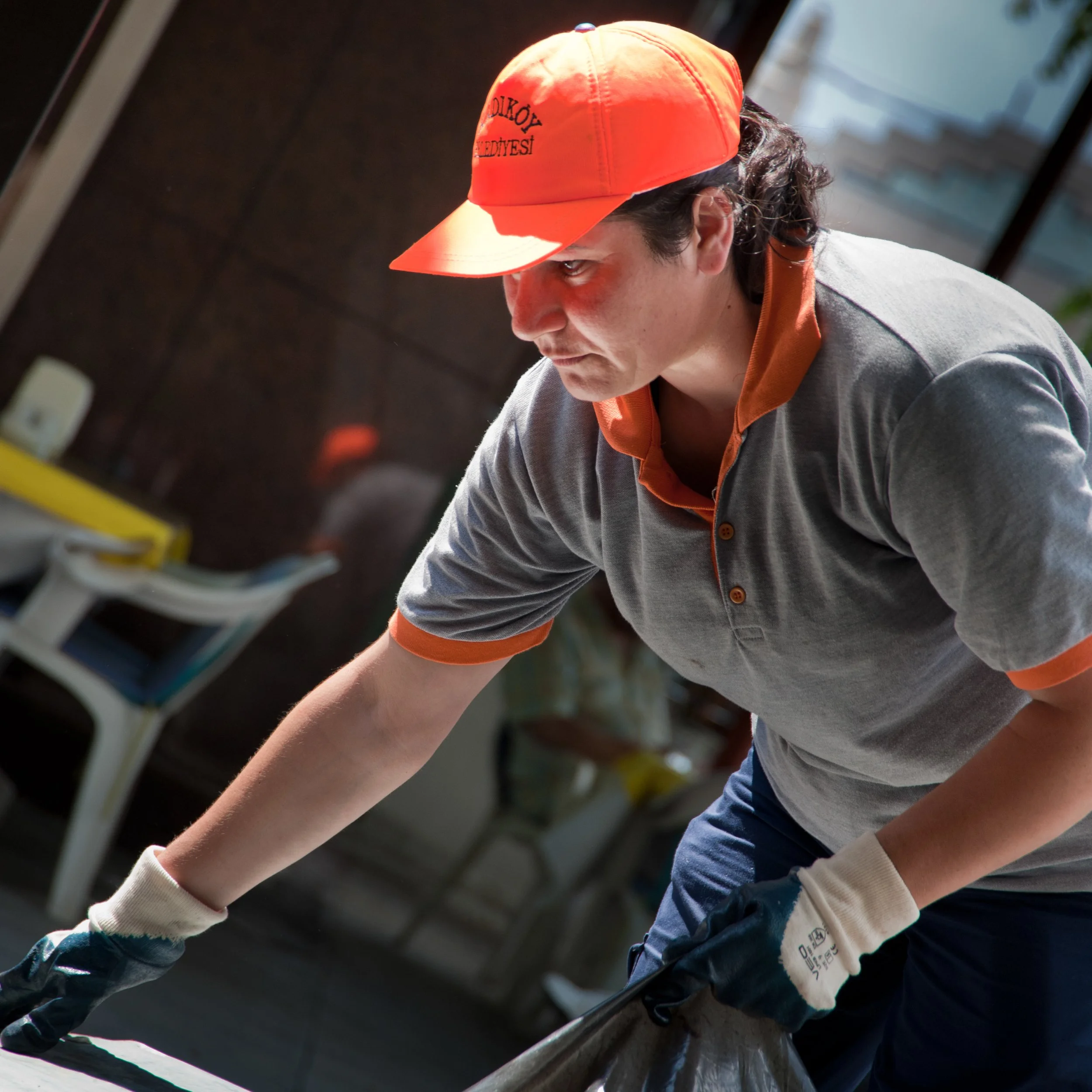 A man wearing a gray uniform, orange cap, and gloves is cleaning or working on a surface in an indoor space.