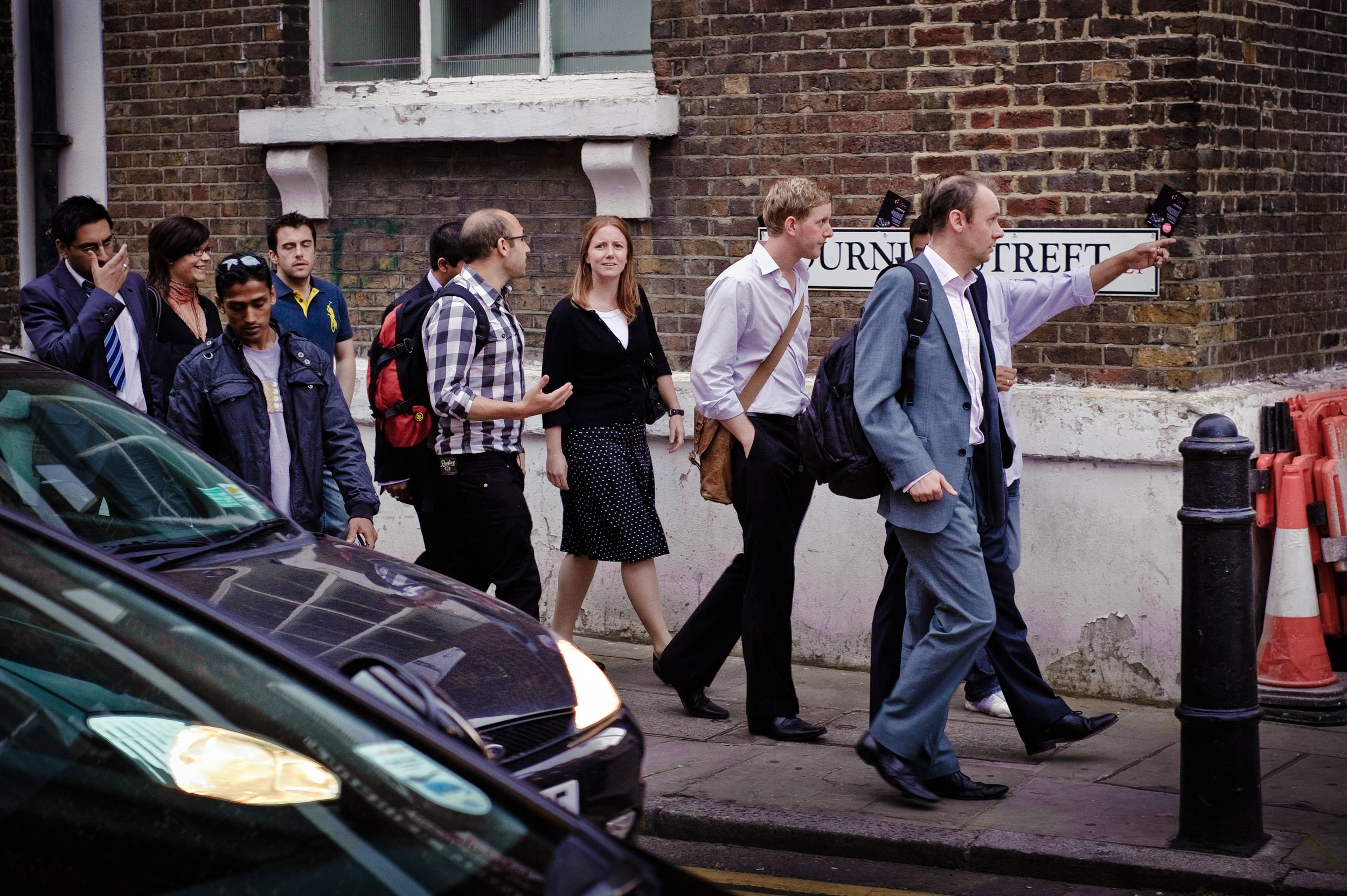 Group of business professionals walking on sidewalk next to brick building and street sign reading "Furnival Street" in London.
