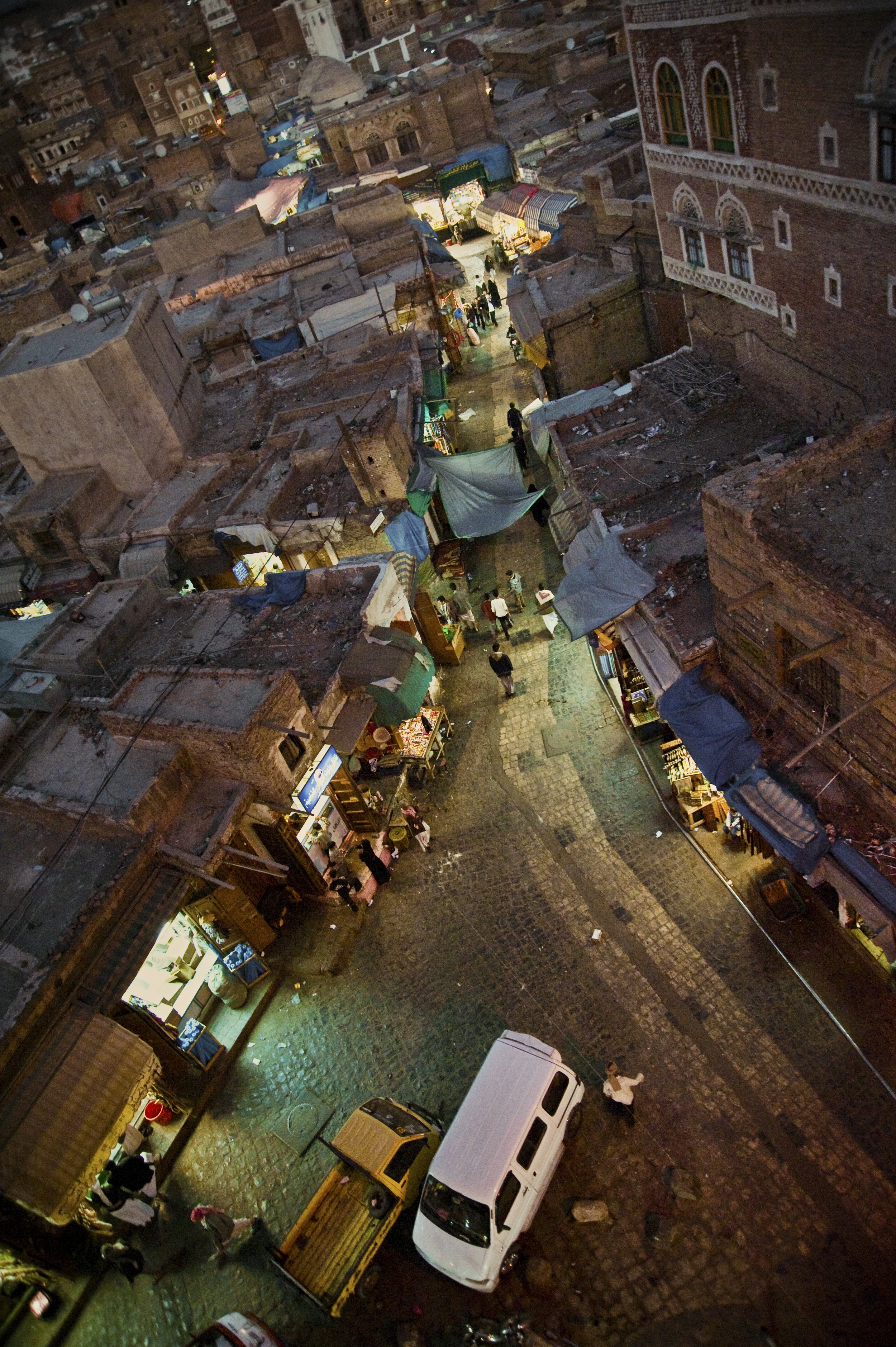 Nighttime street scene with small market stalls, people walking, and buildings with illuminated windows.