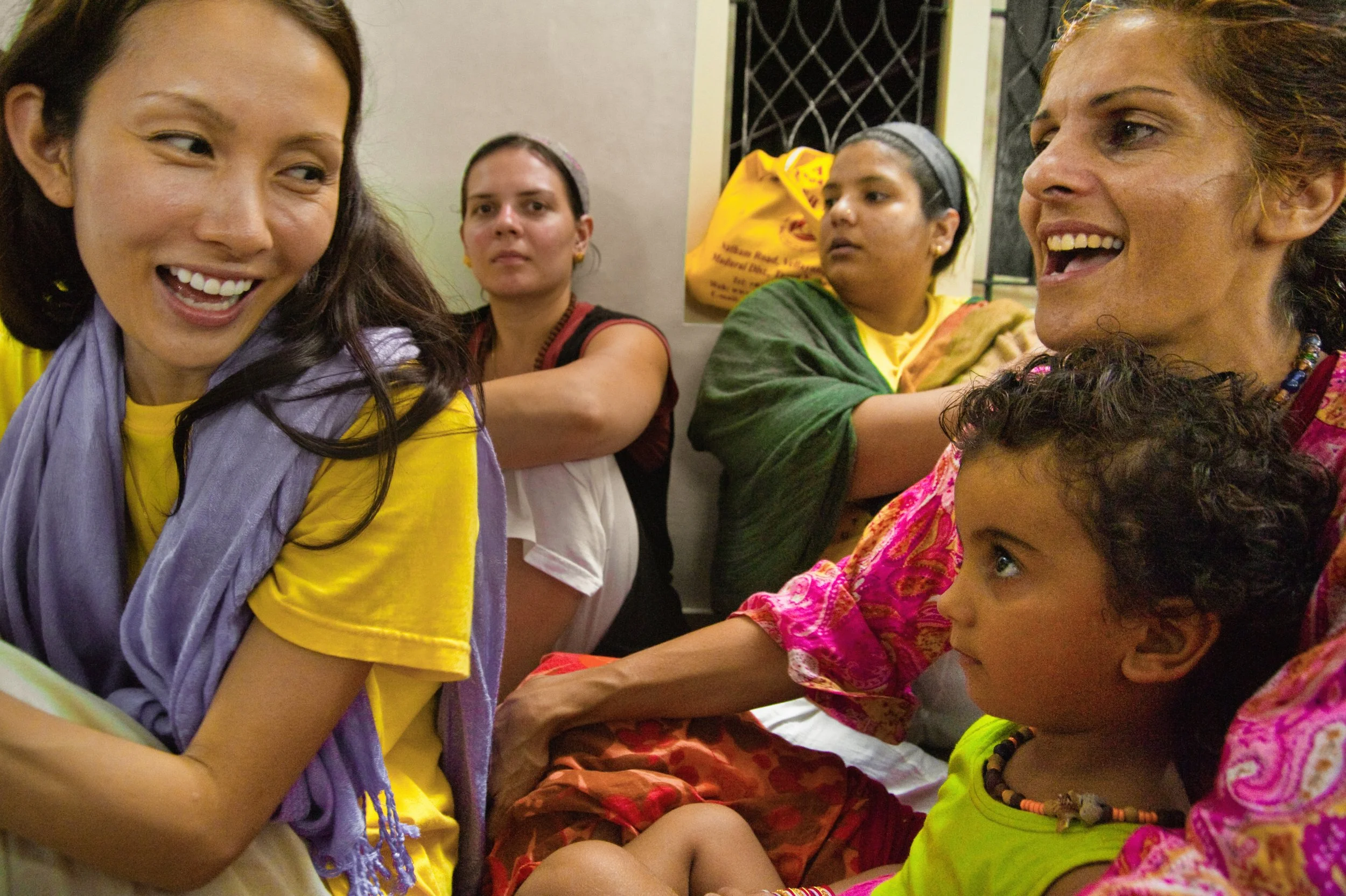 Group of women and a young girl sitting and talking together, some smiling and engaging in conversation.