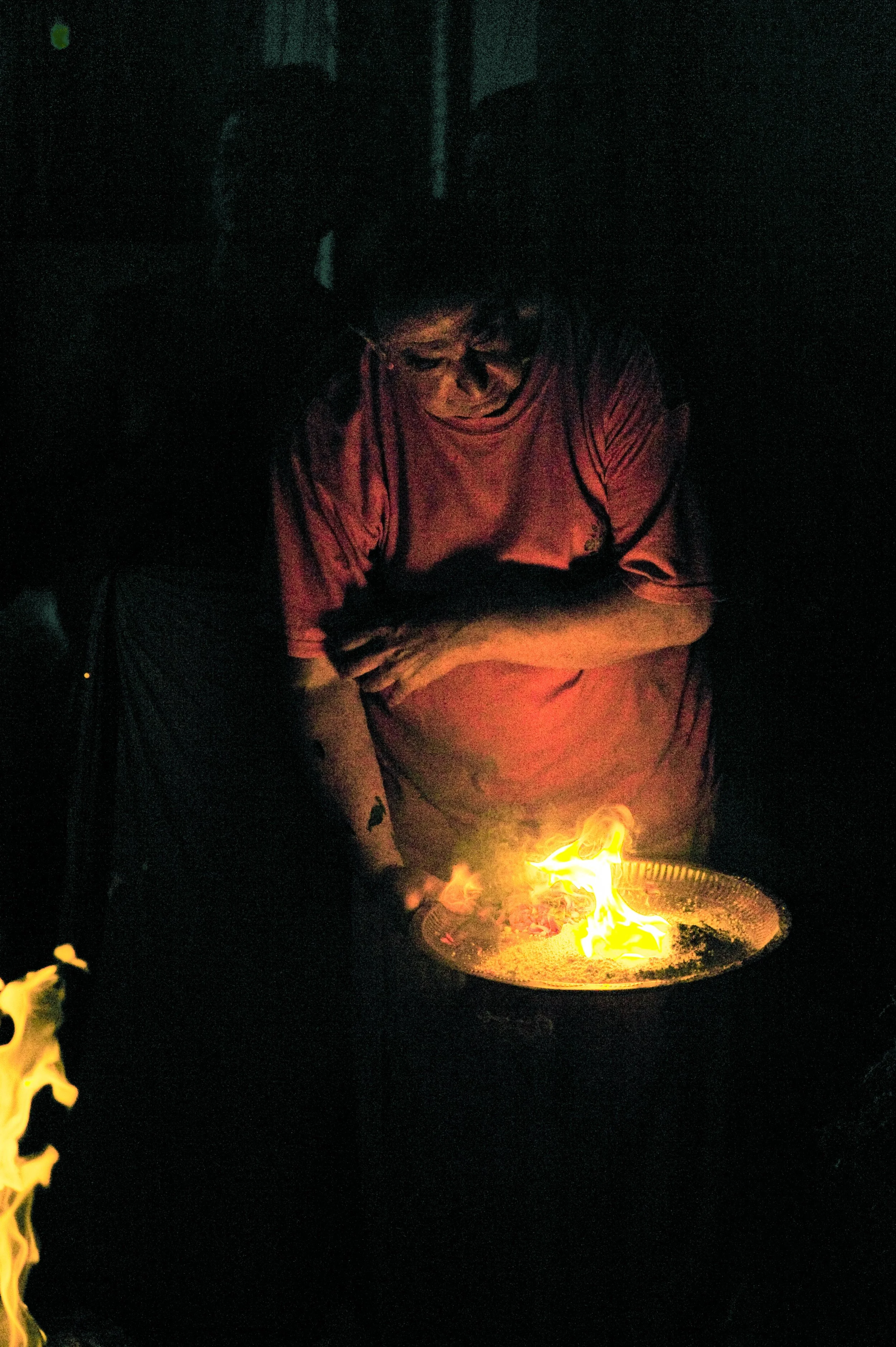 Person in a dimly lit environment looking at a flaming dish or object on a tray.