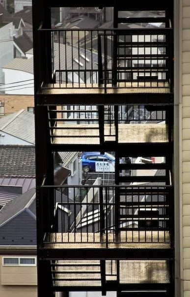 Outdoor metal staircase with three levels, surrounded by residential rooftops and brick buildings.