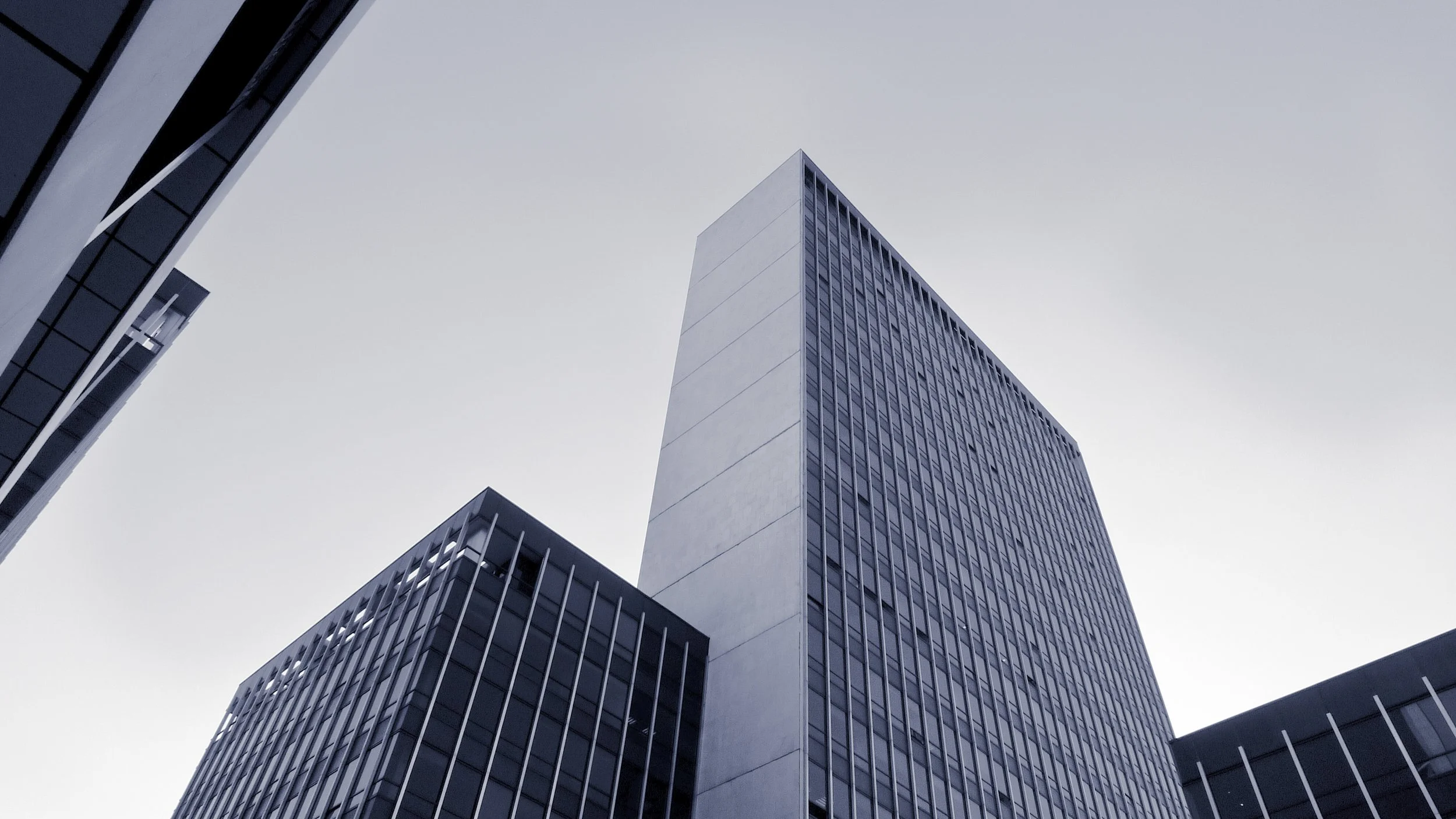 Low-angle view of modern office skyscrapers with glass facades against a pale sky.