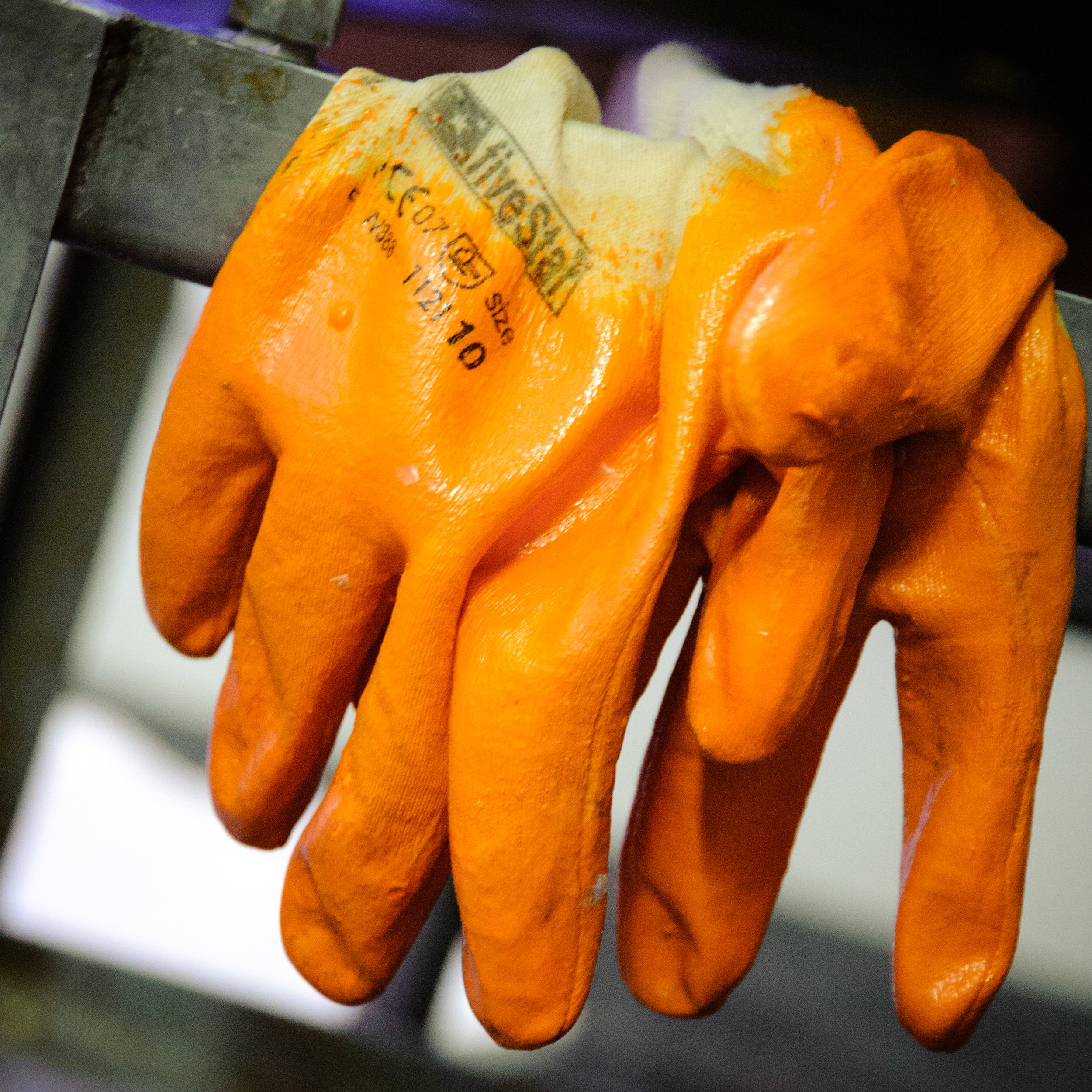 Close-up of a pair of orange work gloves hanging on a metal hook.