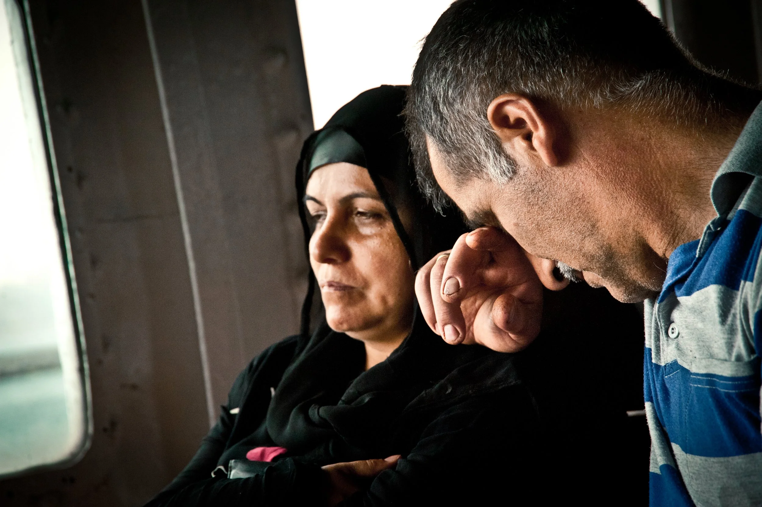 A man and woman sitting side by side; the woman appears to be sad or thoughtful, resting her head on her hand, while the man looks downward with his eyes closed, in a somber mood.