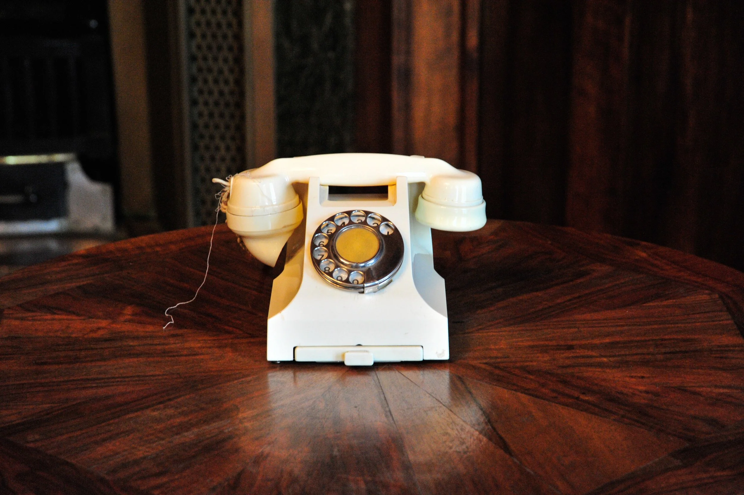 An antique cream-colored rotary dial telephone on a wooden table with a dark wood-paneled background.