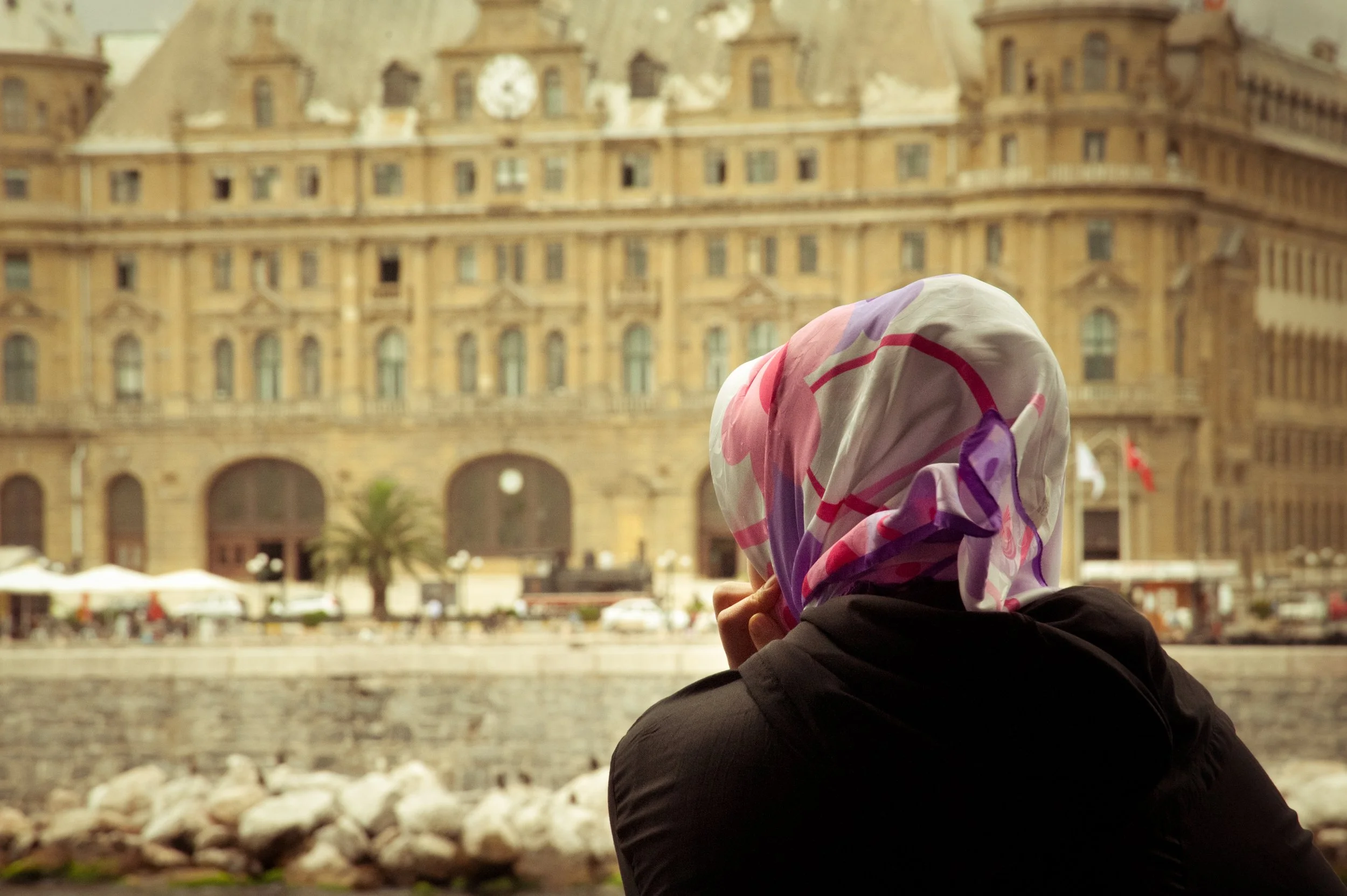 Person wearing a colorful scarf looking at a historic building by a waterway.