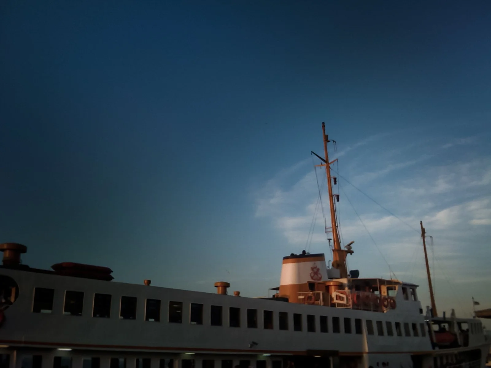 A ship docked at a port during sunset with a clear blue sky and some wispy clouds.