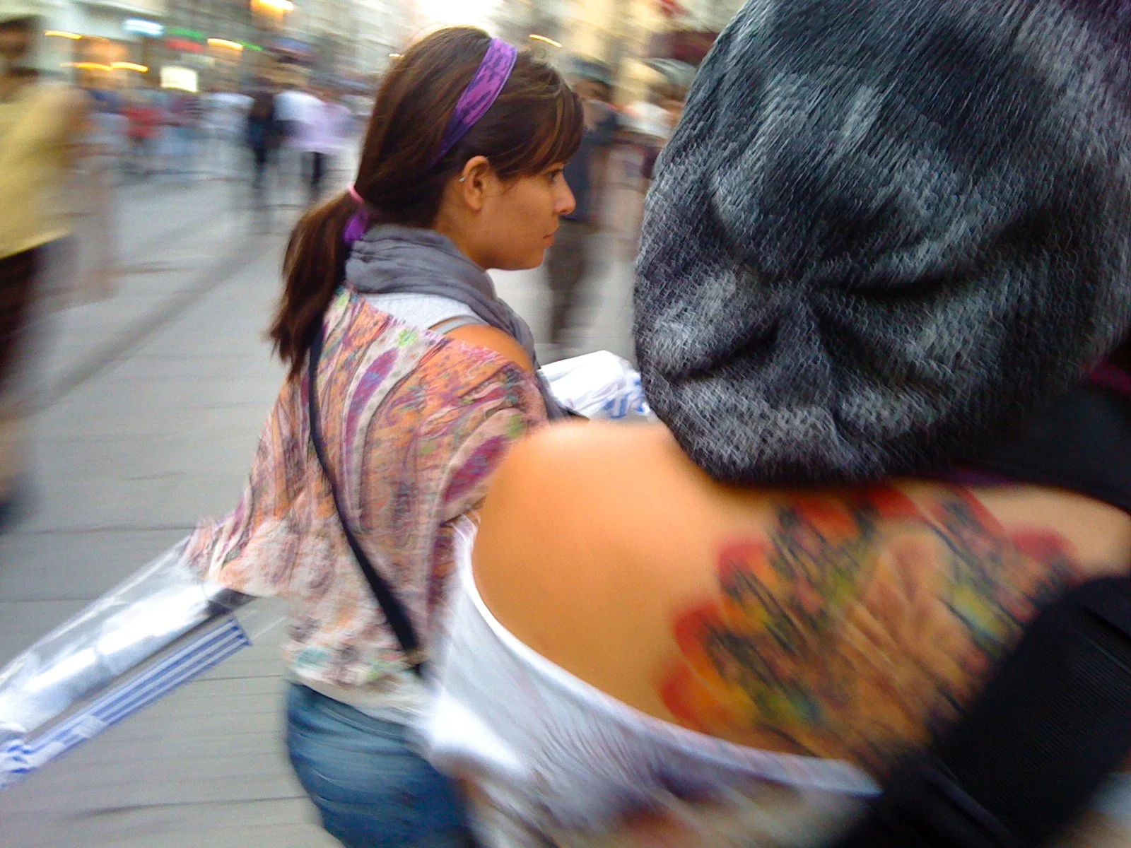 A woman with a purple headband and a colorful shirt is walking in a busy, blurred city street.