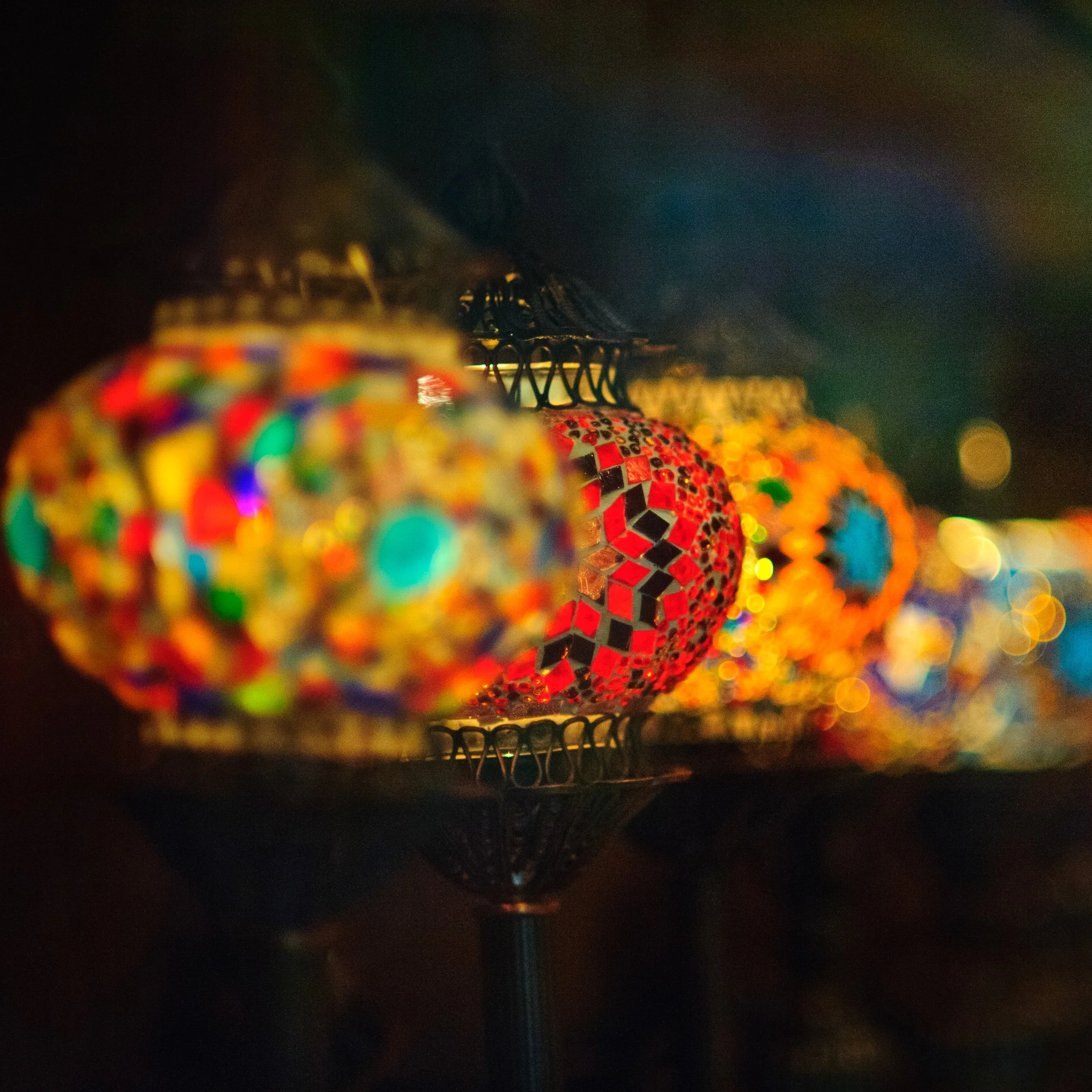 Colorful mosaic glass lanterns hanging against a dark background, illuminated softly.
