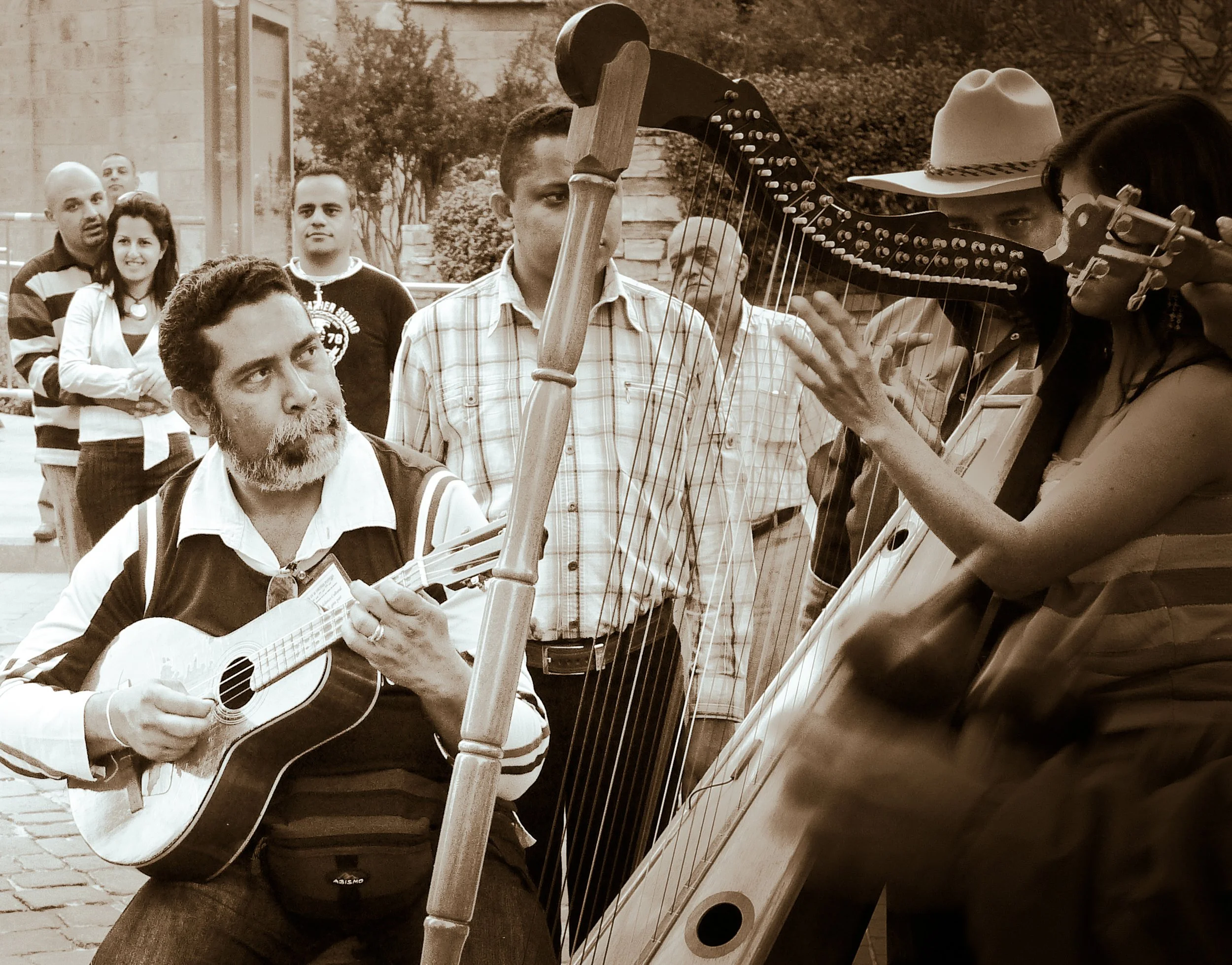 A street performer playing guitar and a woman playing a harp, with a group of people watching in the background.