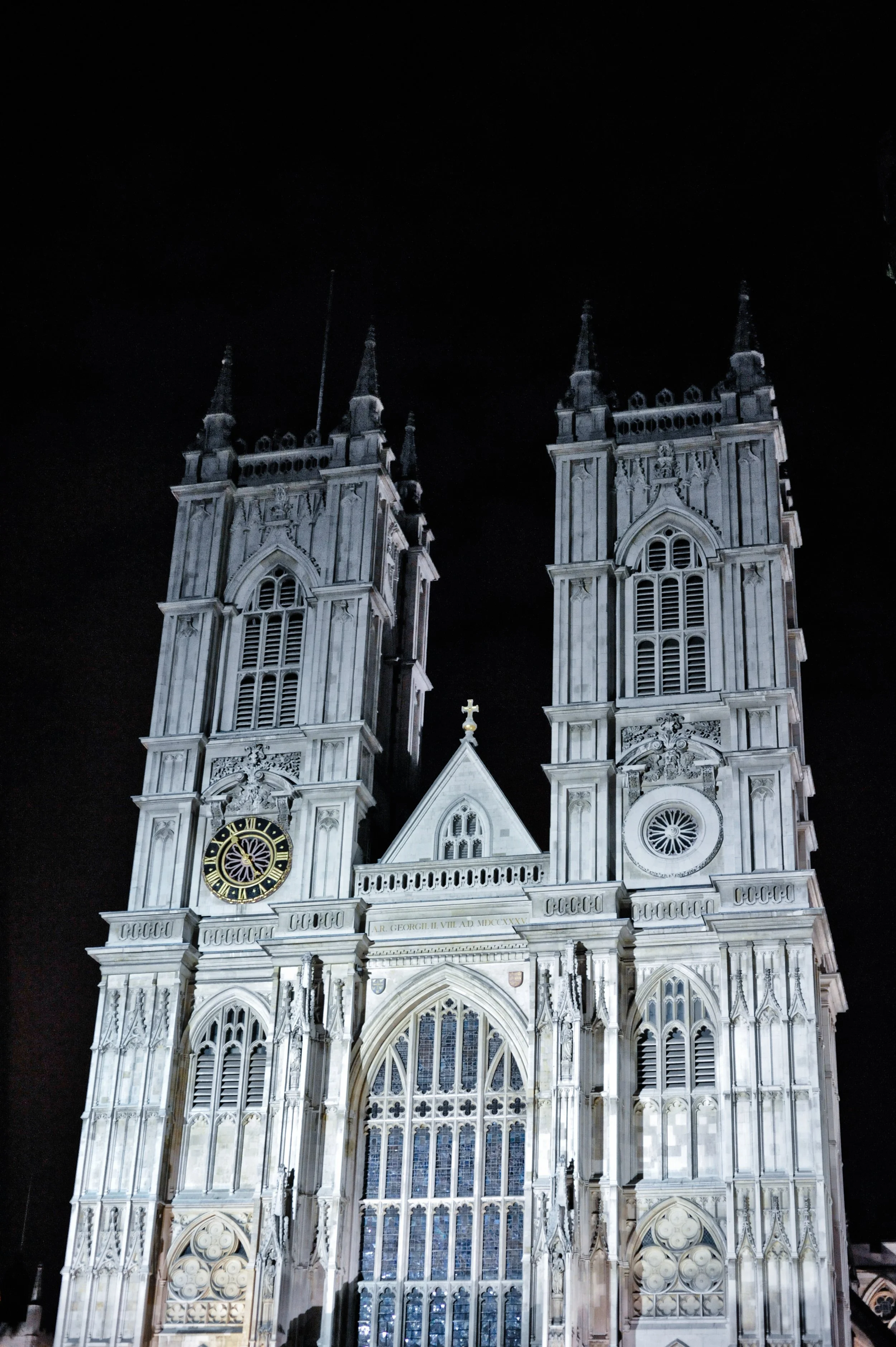 Night view of Westminster Abbey's facade with illuminated Gothic architecture and twin towers against a dark sky.