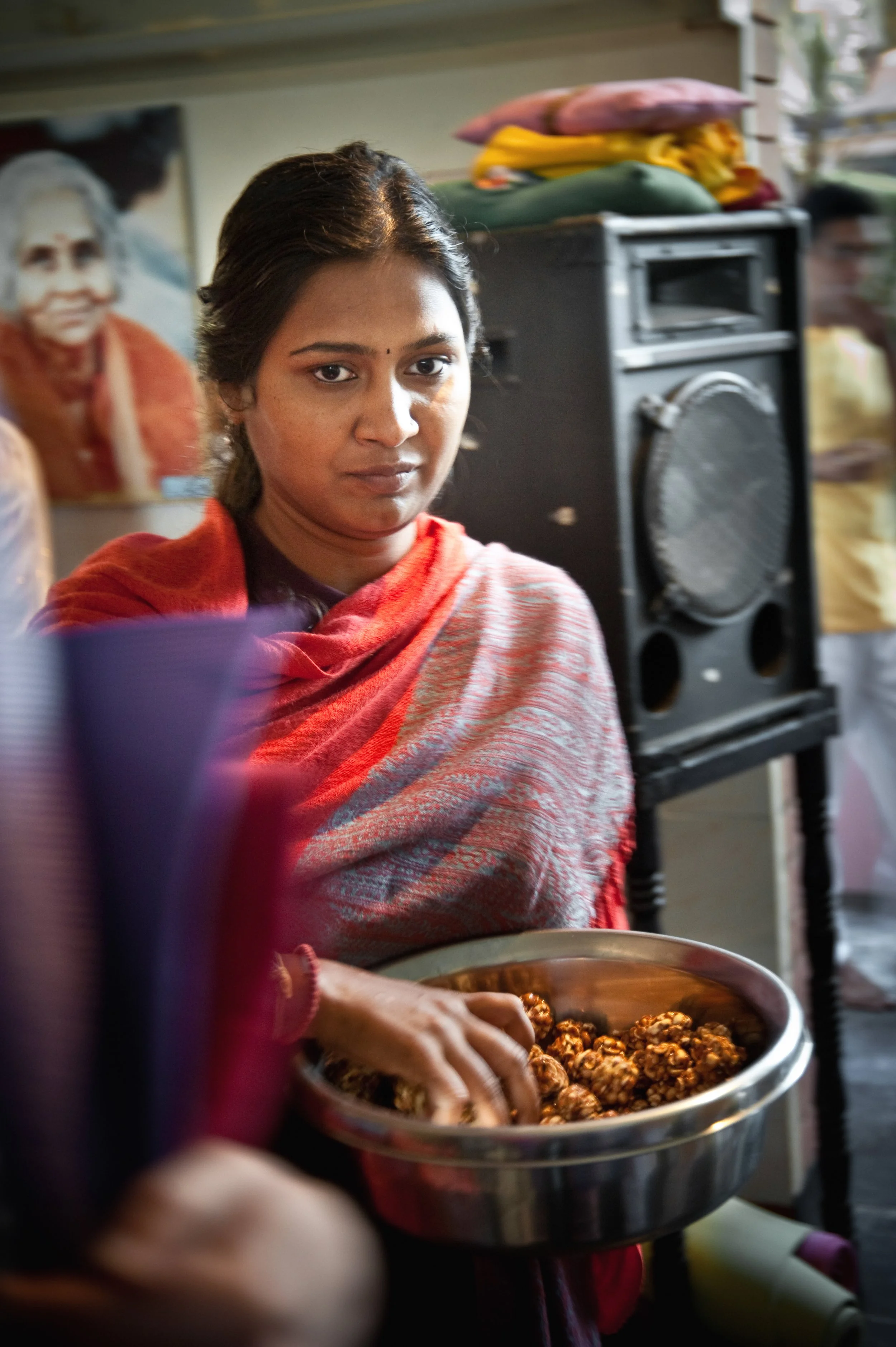 A woman in traditional Indian attire holding a bowl of sweets at an indoor gathering