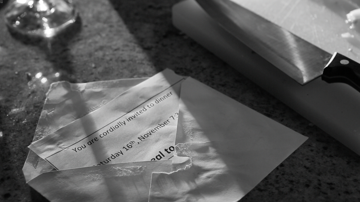 Torn invitation or RSVP card on a kitchen countertop alongside a chef's knife, with a wine glass in the background.