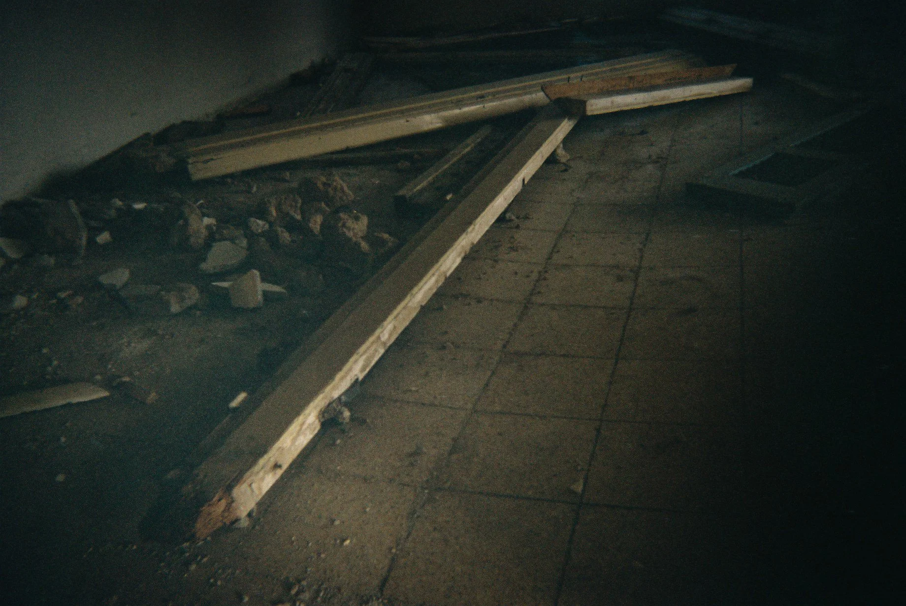 Construction materials and debris on a dirty floor, including wooden planks, rocks, and broken tiles.