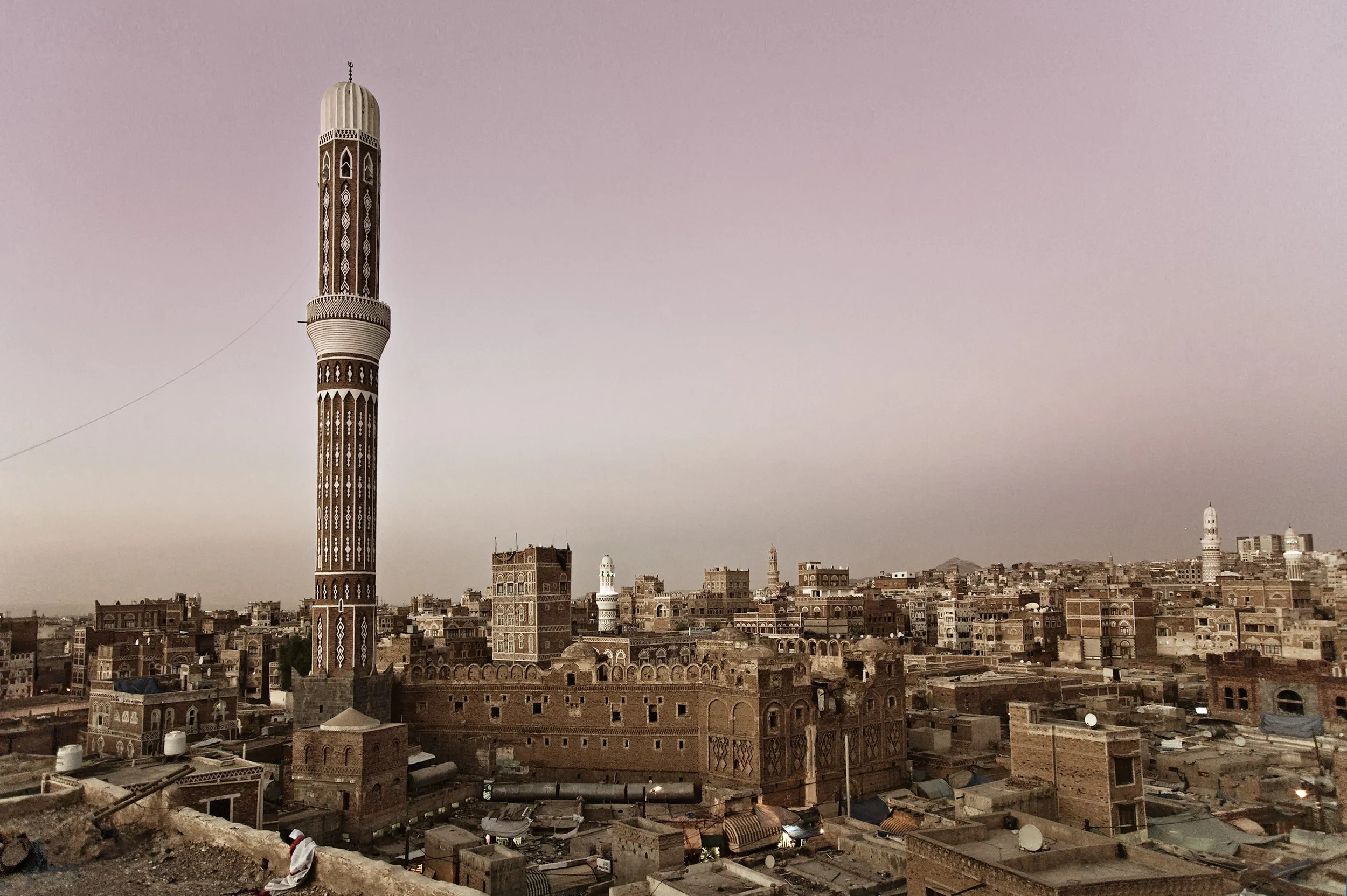 Cityscape featuring a tall minaret, traditional Middle Eastern buildings, and a hazy sky.