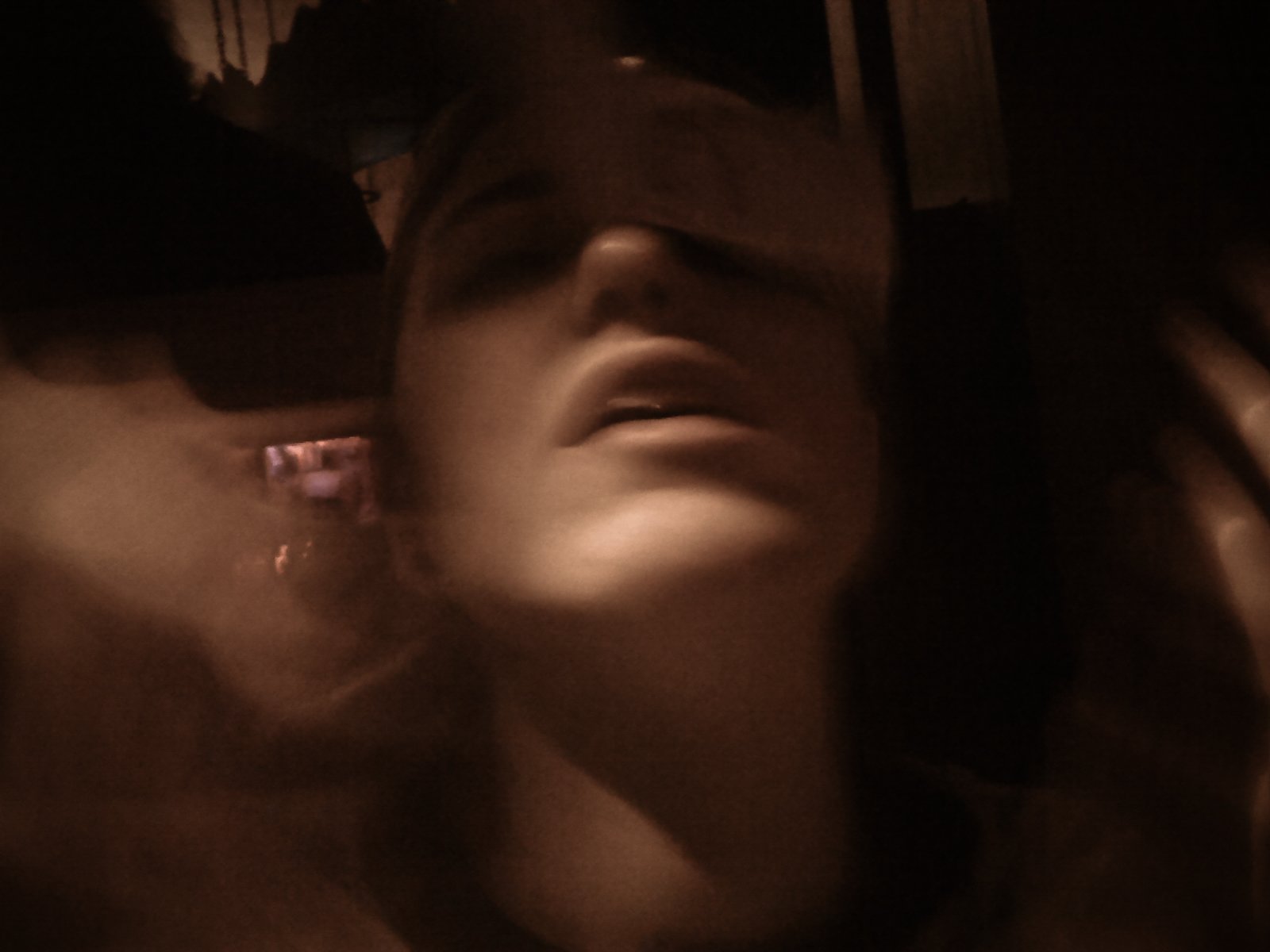 A woman with long hair and sunglasses, leaning back with her head tilted, in a dark setting.