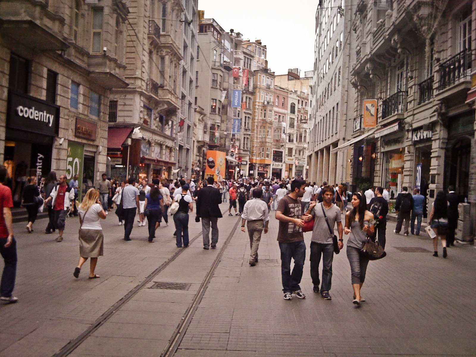 Street scene in a busy city with pedestrians walking among tall buildings, shops, and advertisements.