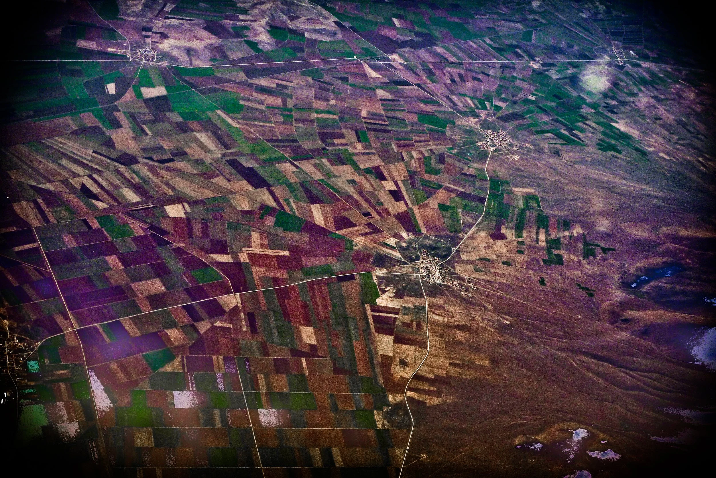 An aerial view of a rural landscape with a patchwork of agricultural fields, roads, and small settlements, taken at night from space.