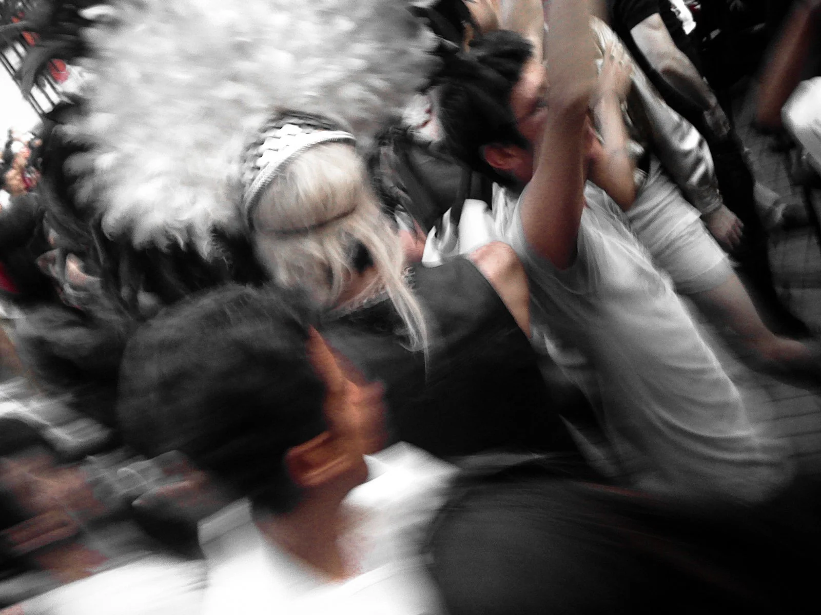 People in a crowded space, some wearing masks and protective gear, with a sense of movement and chaos.