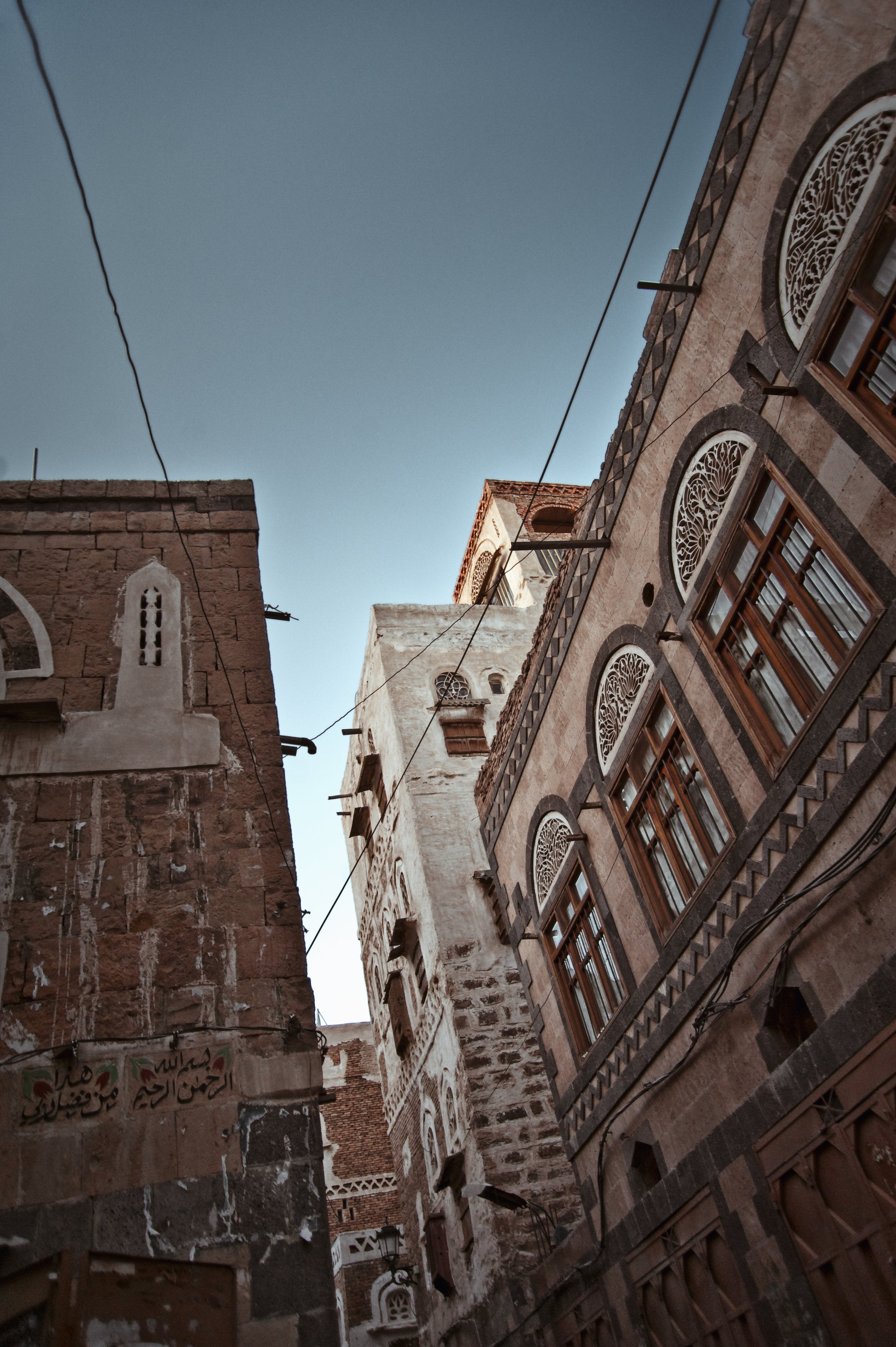 Low angle view of historic buildings with ornate windows and stone facades in a narrow alley under a clear blue sky.