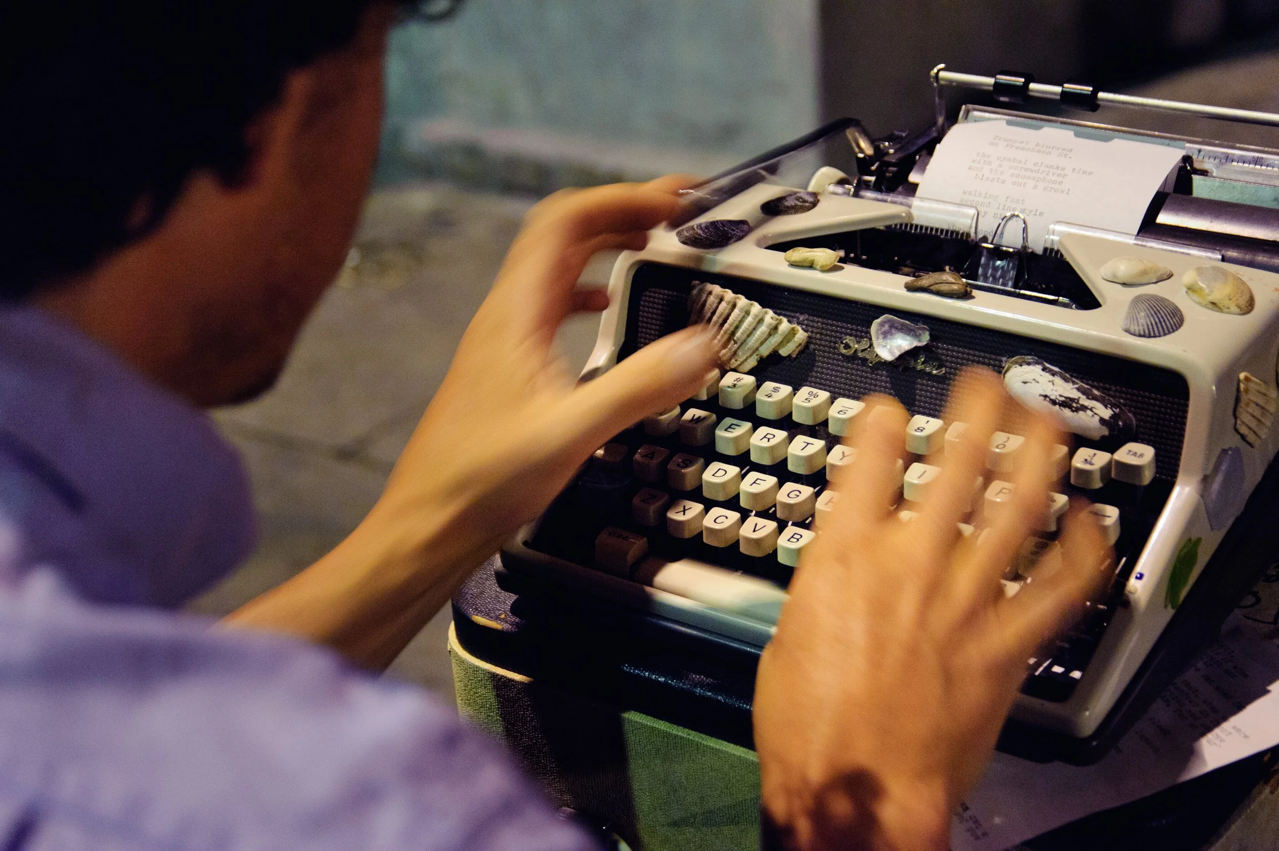 Person typing on a vintage typewriter decorated with shells and small stones.