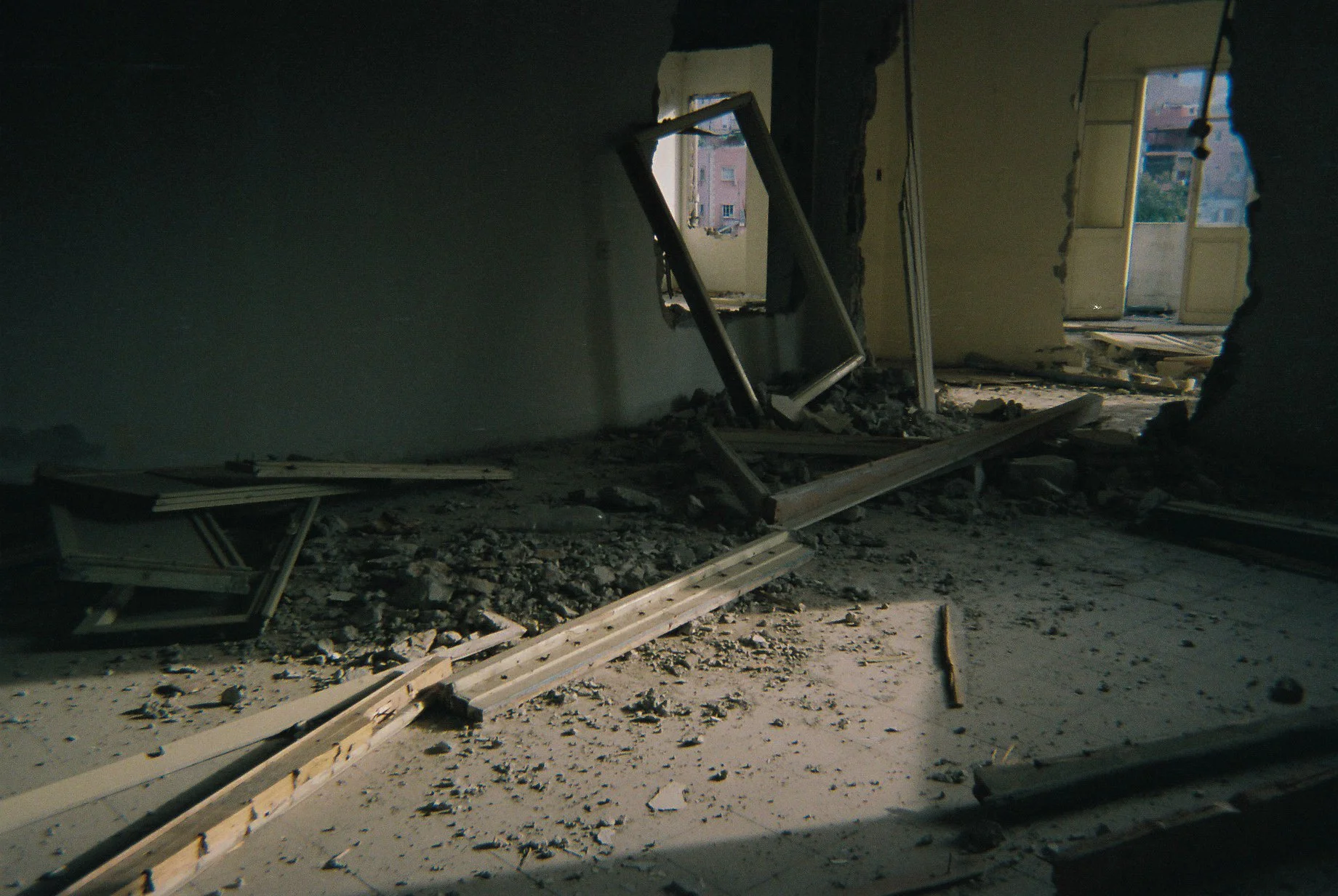 Interior of a damaged building with broken windows, debris, and rubble on the floor.