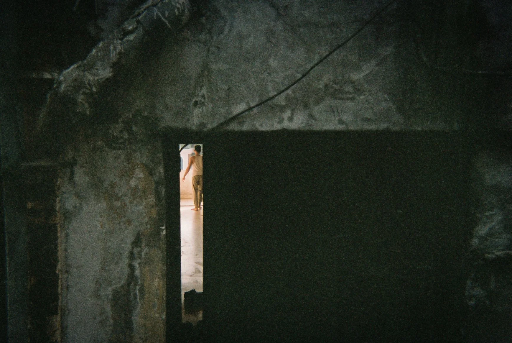 A person walking through a doorway inside a dark, concrete space, possibly a basement or cellar.