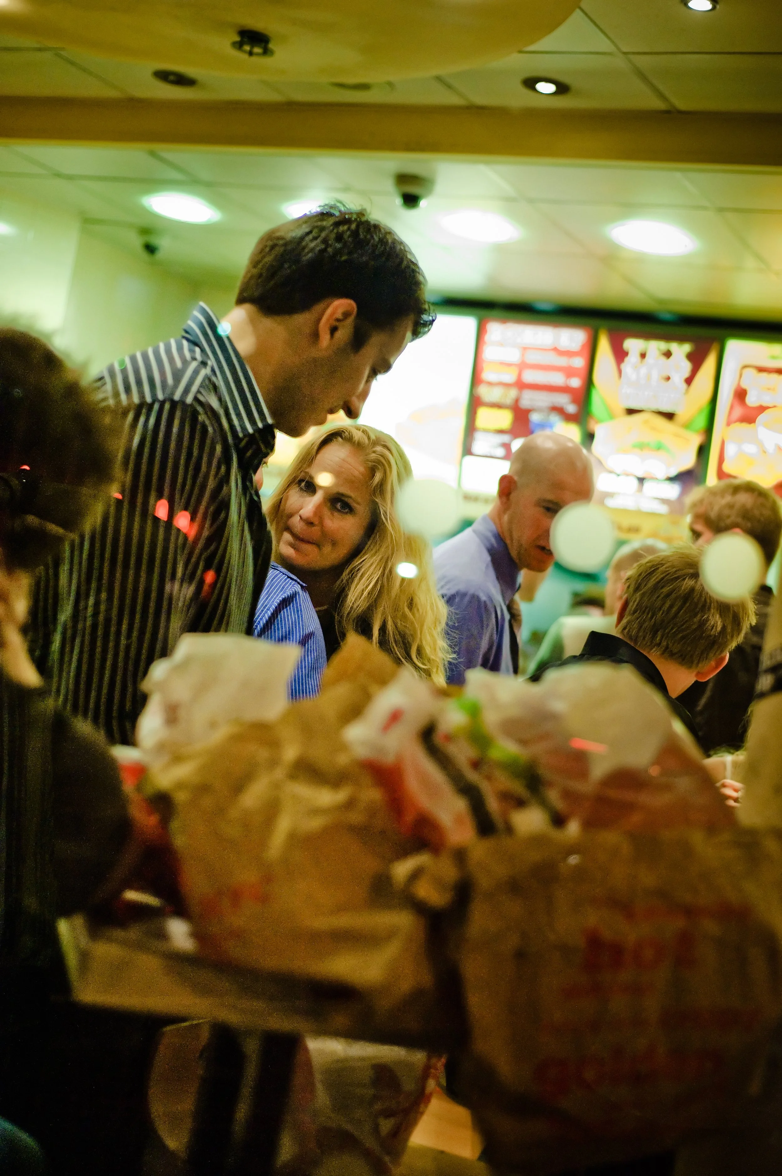 People standing in line at a fast food restaurant, with a menu board visible in the background.