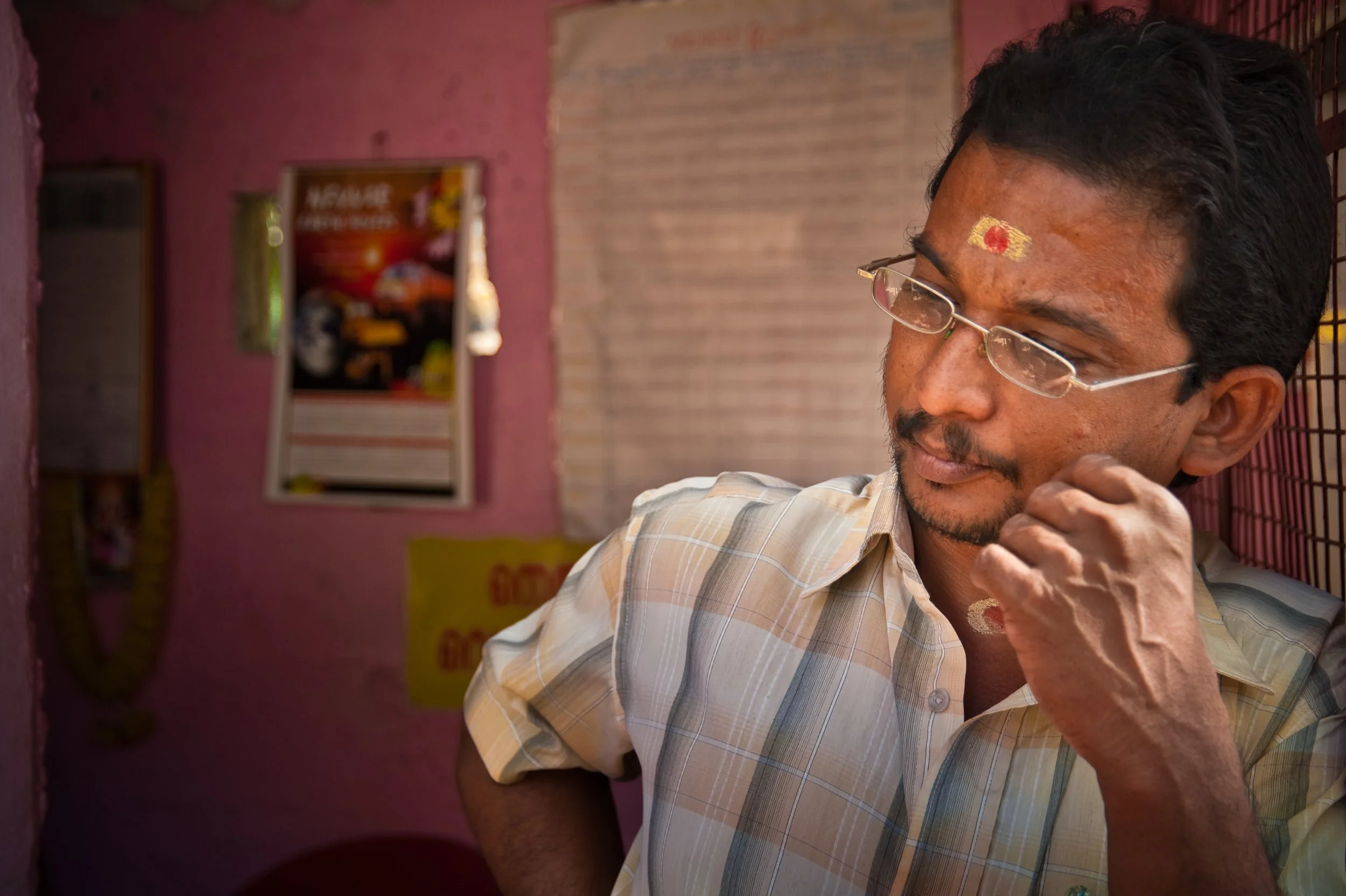 Man adjusting glasses inside a pink-walled room with posters on the wall.