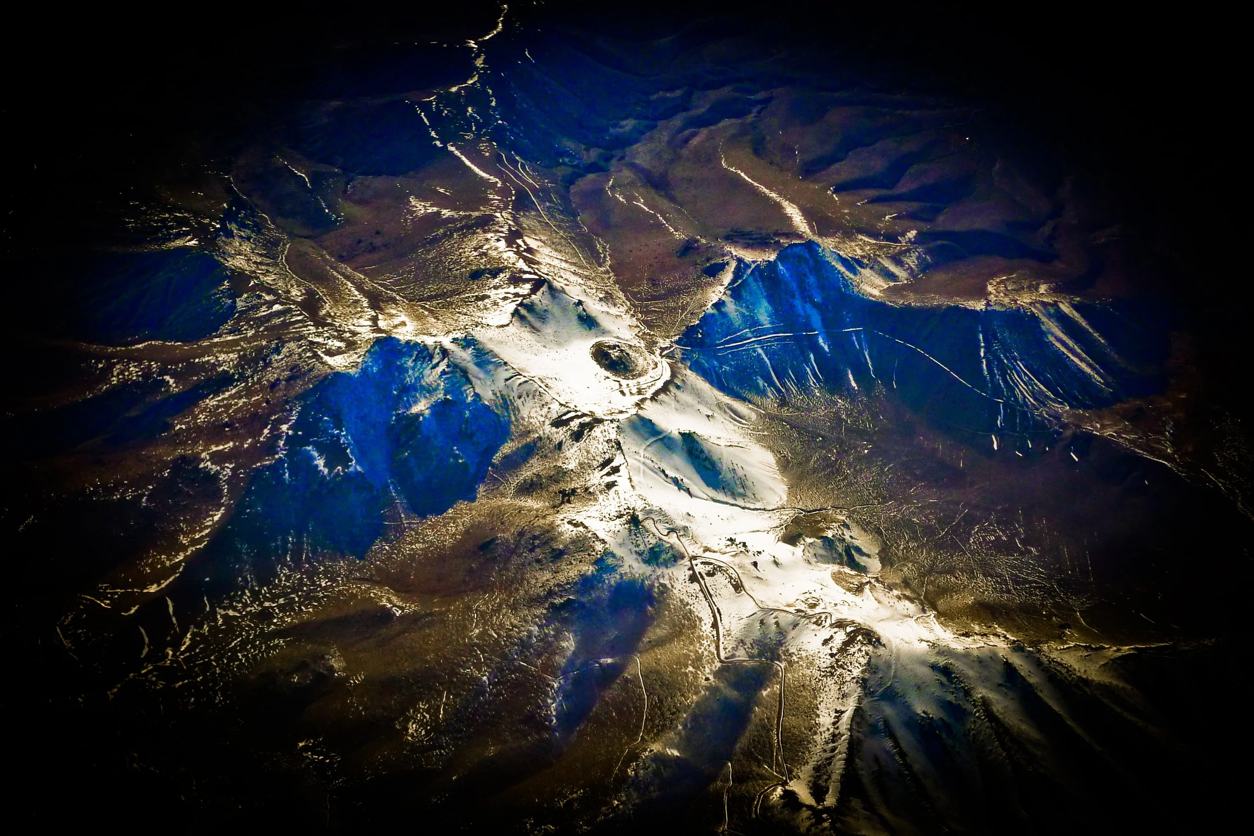 An aerial view of Mount Saint Helens volcano with snow on its slopes, center crater, and surrounding rugged landscape at night.